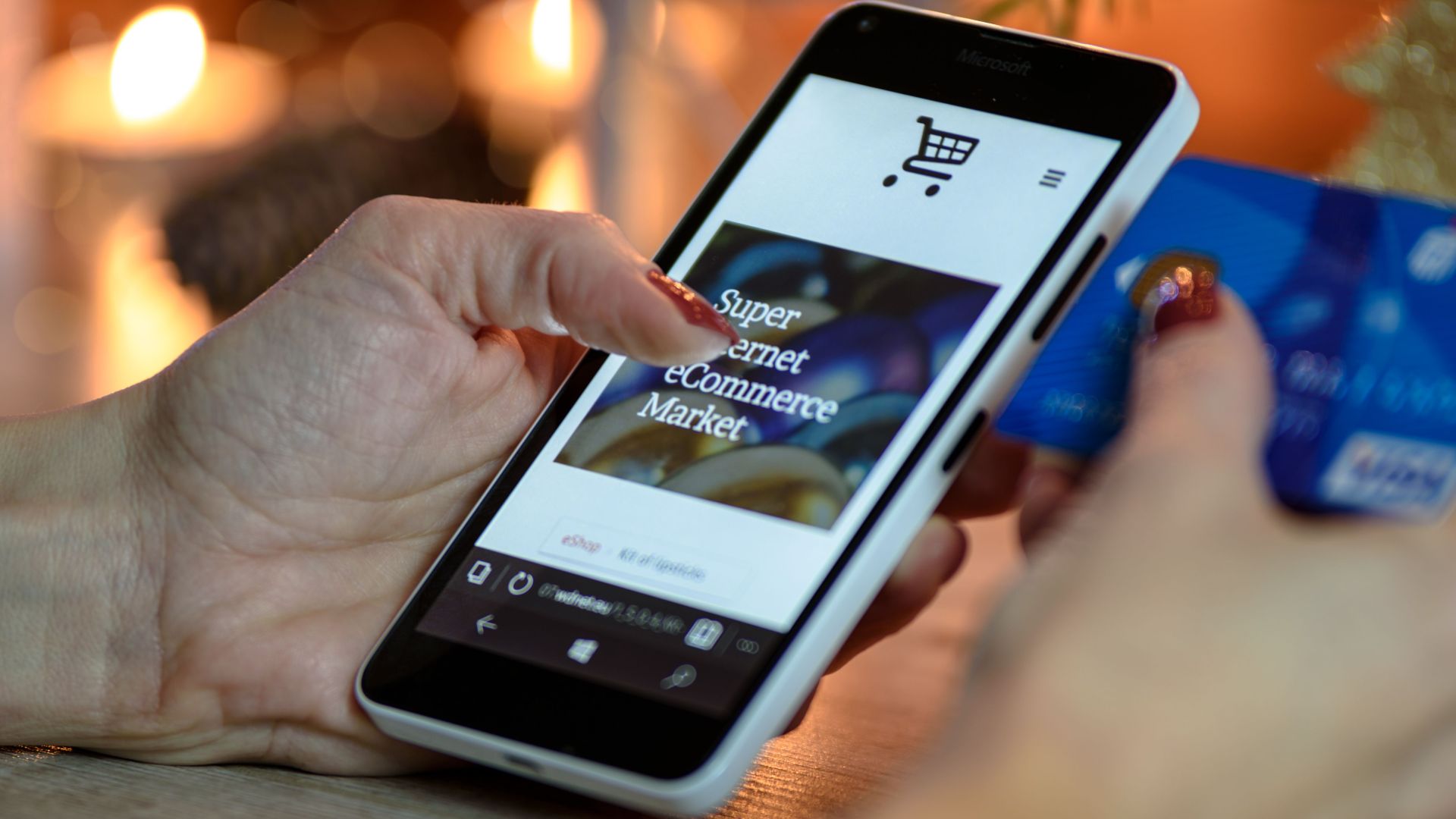 Woman using smartphone for online shopping with credit card in hand, festive background lighting.