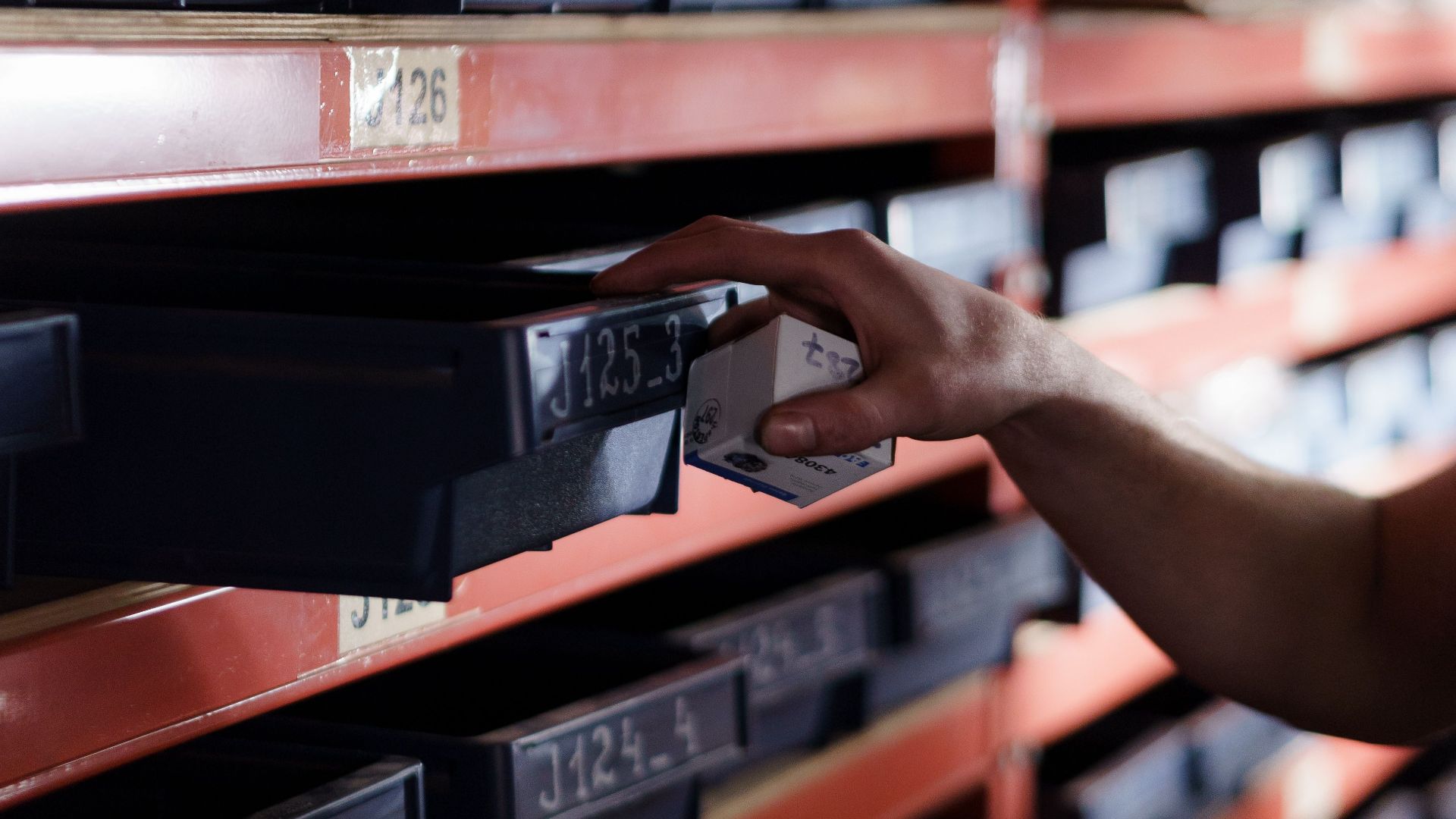 Hand reaching for storage bin in organized warehouse shelving. Perfect for logistics and inventory themes.
