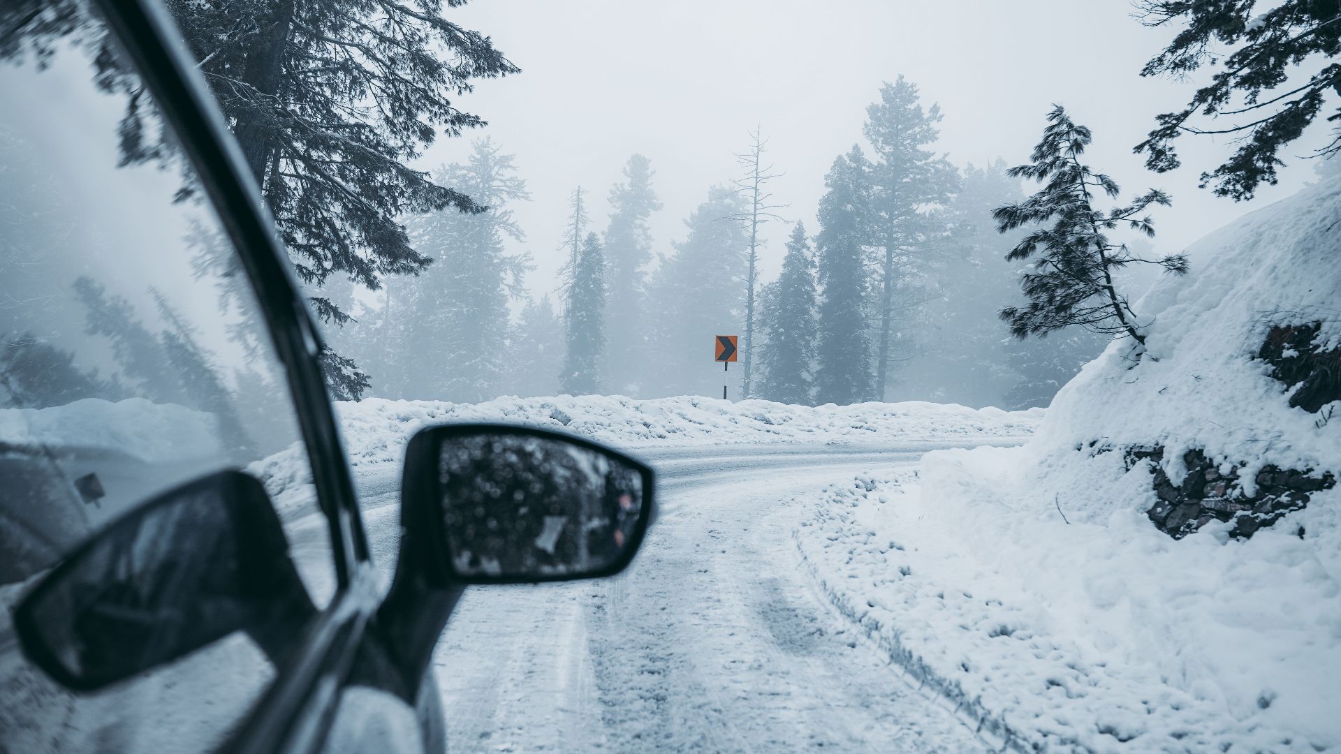 A car drives through a foggy snow-covered mountain road, capturing winter's serene beauty.