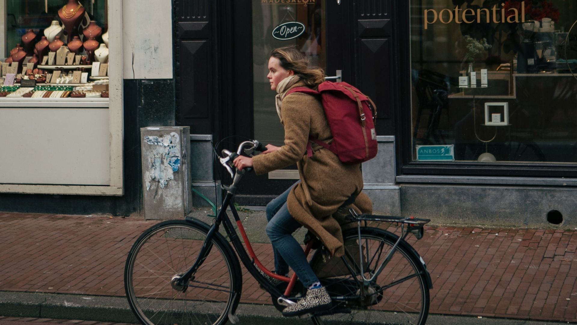 A woman riding a bicycle on an urban street past shops and cafes during the day.