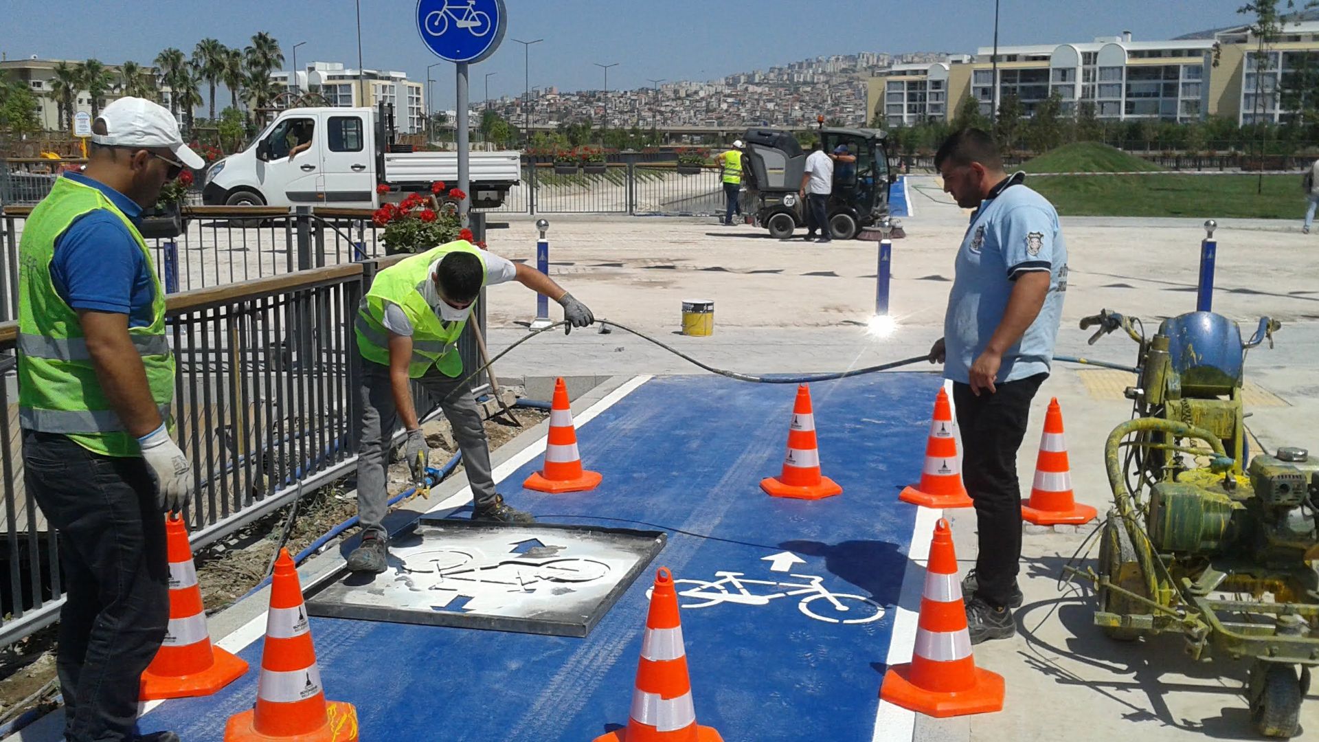 Full body road workers wearing uniforms and high visibility vests marking cycle lane with white paint on sunny weather