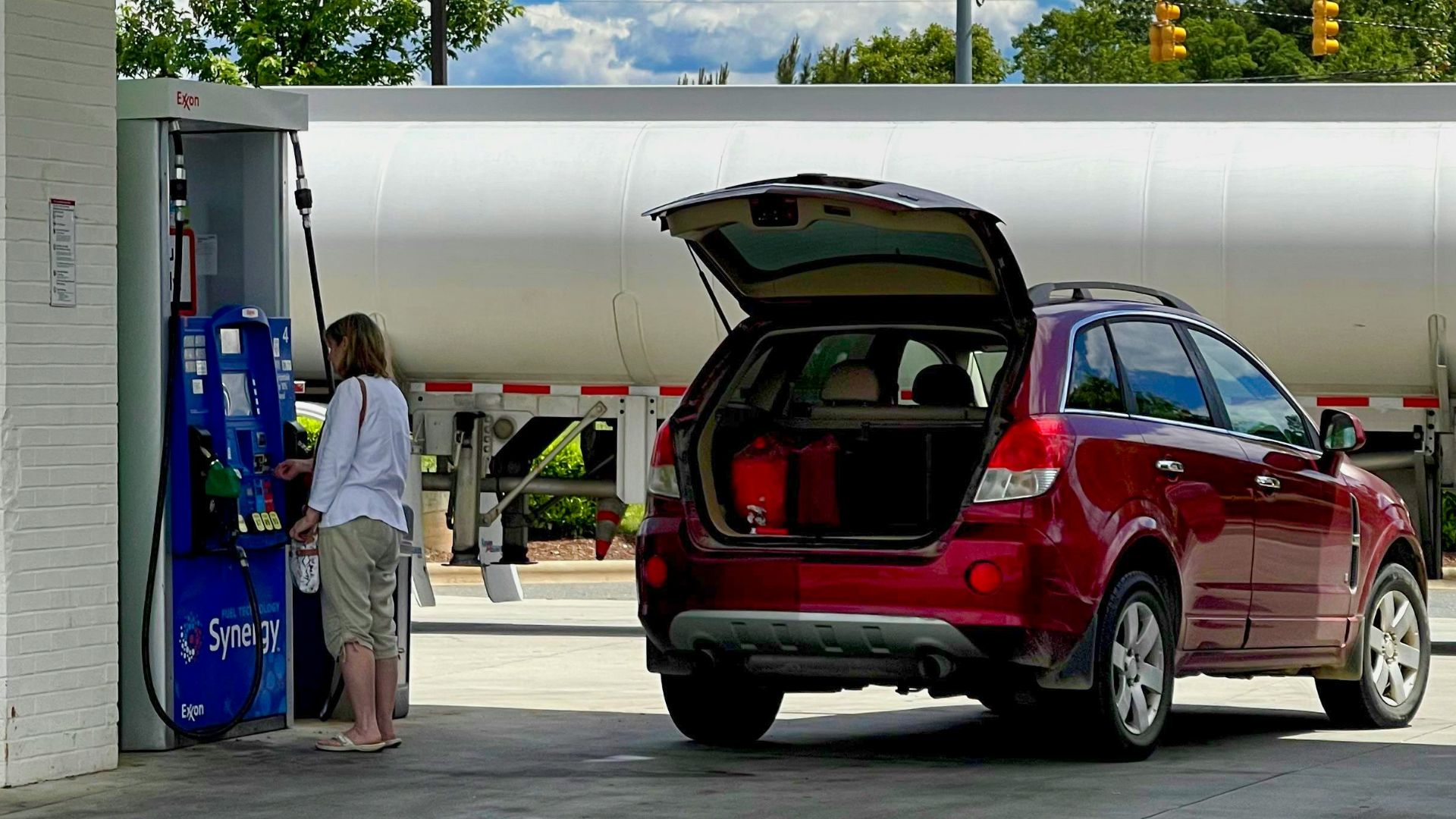 man in white t-shirt standing beside red suv during daytime