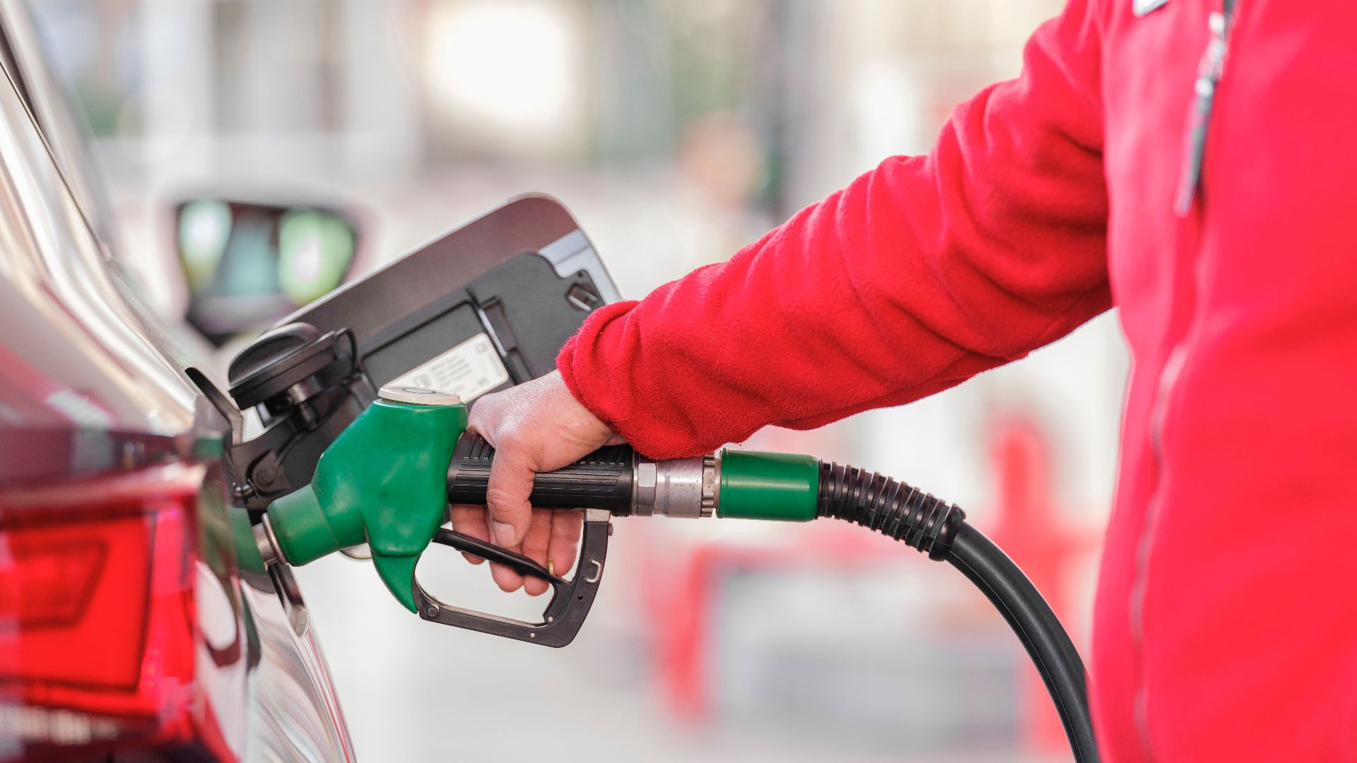 Close-up of a person refueling a car with a green hose at a gas station.