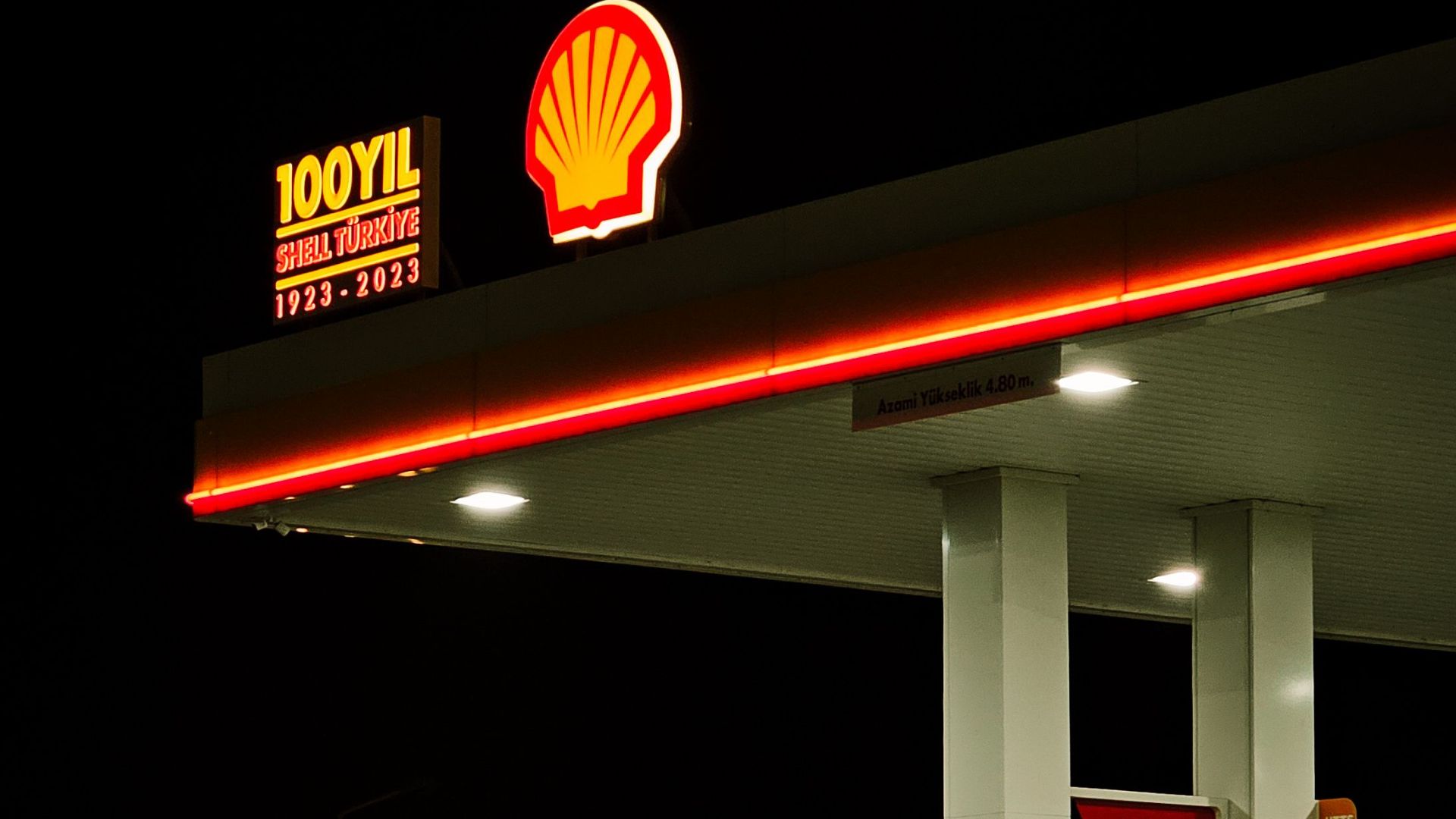 A Shell gas station illuminated by neon lights in a dark night setting, offering a moody atmosphere.