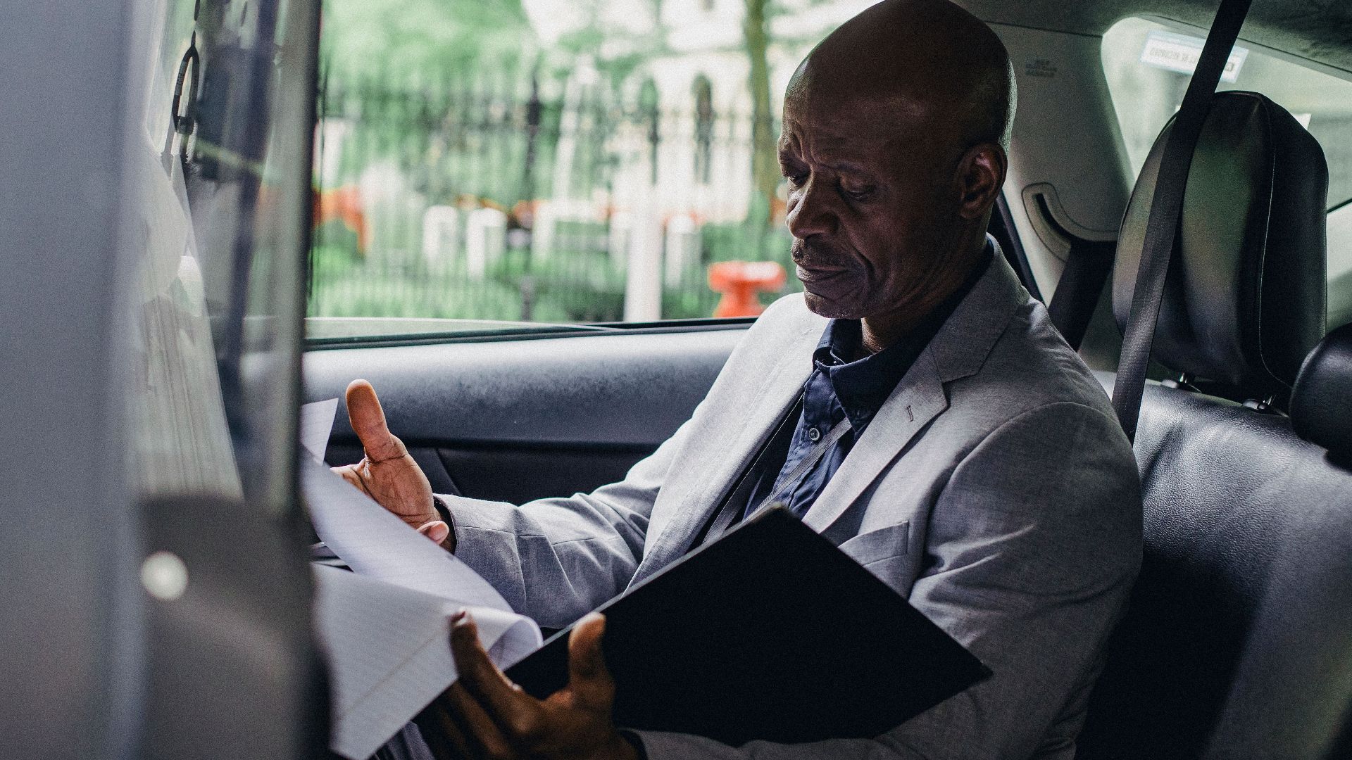 Side view of African American male in elegant suit checking folder of documents in automobile