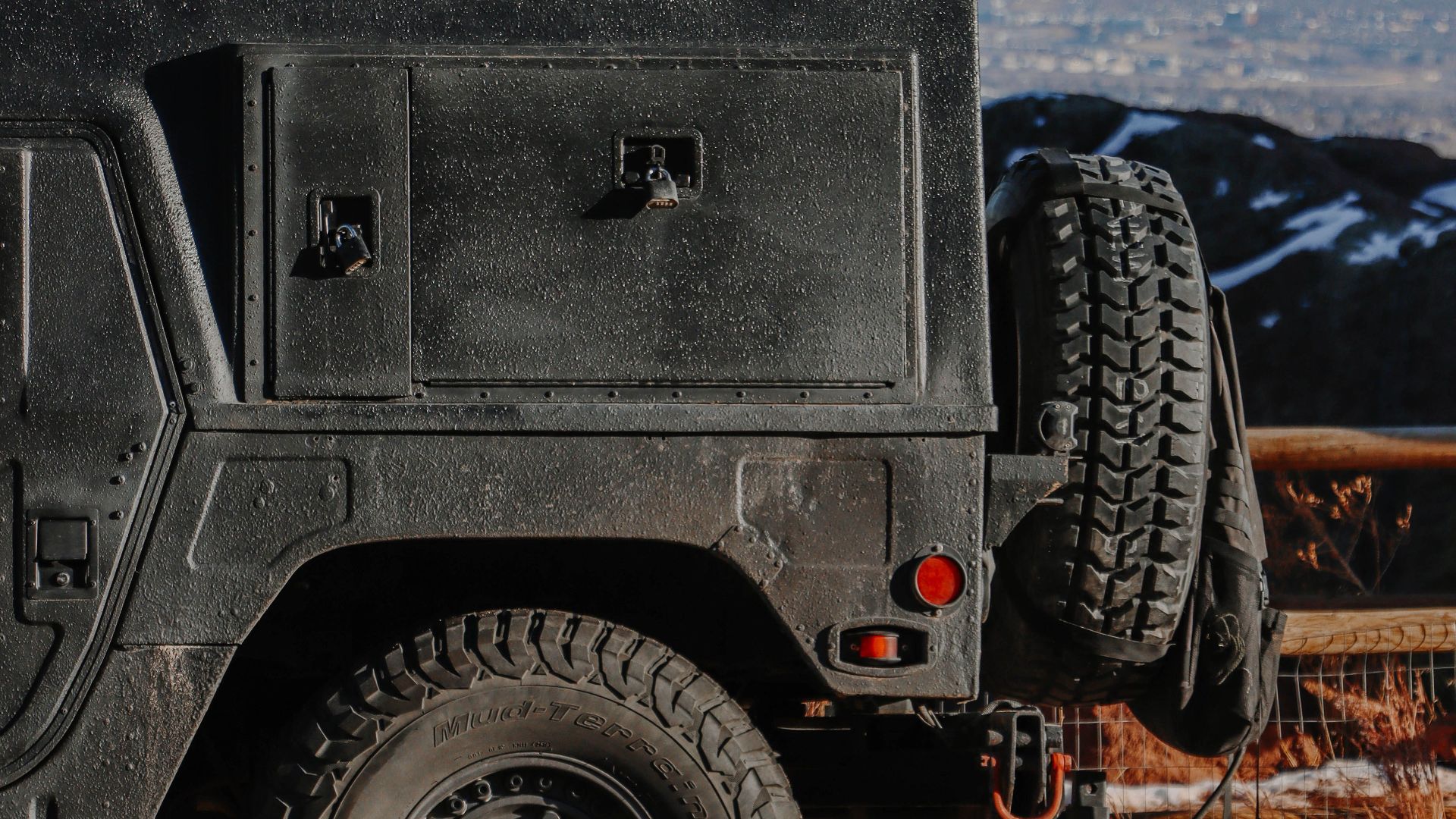 Black 4x4 vehicle with spare tire parked on a road with mountain view.