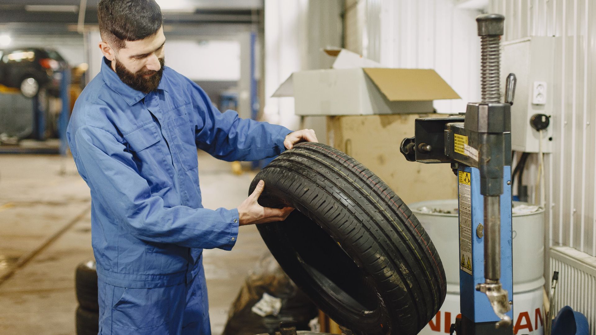 Mechanic in blue uniform examining a tire in an automotive garage.