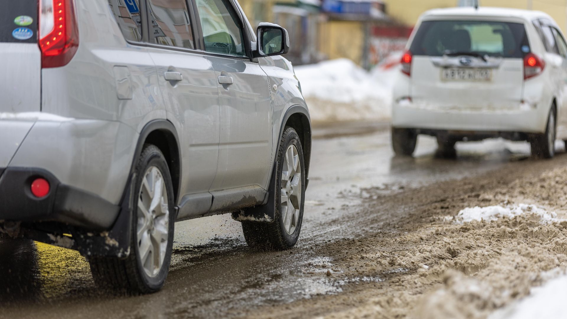 Two cars driving cautiously on a slushy, snowy road during winter.