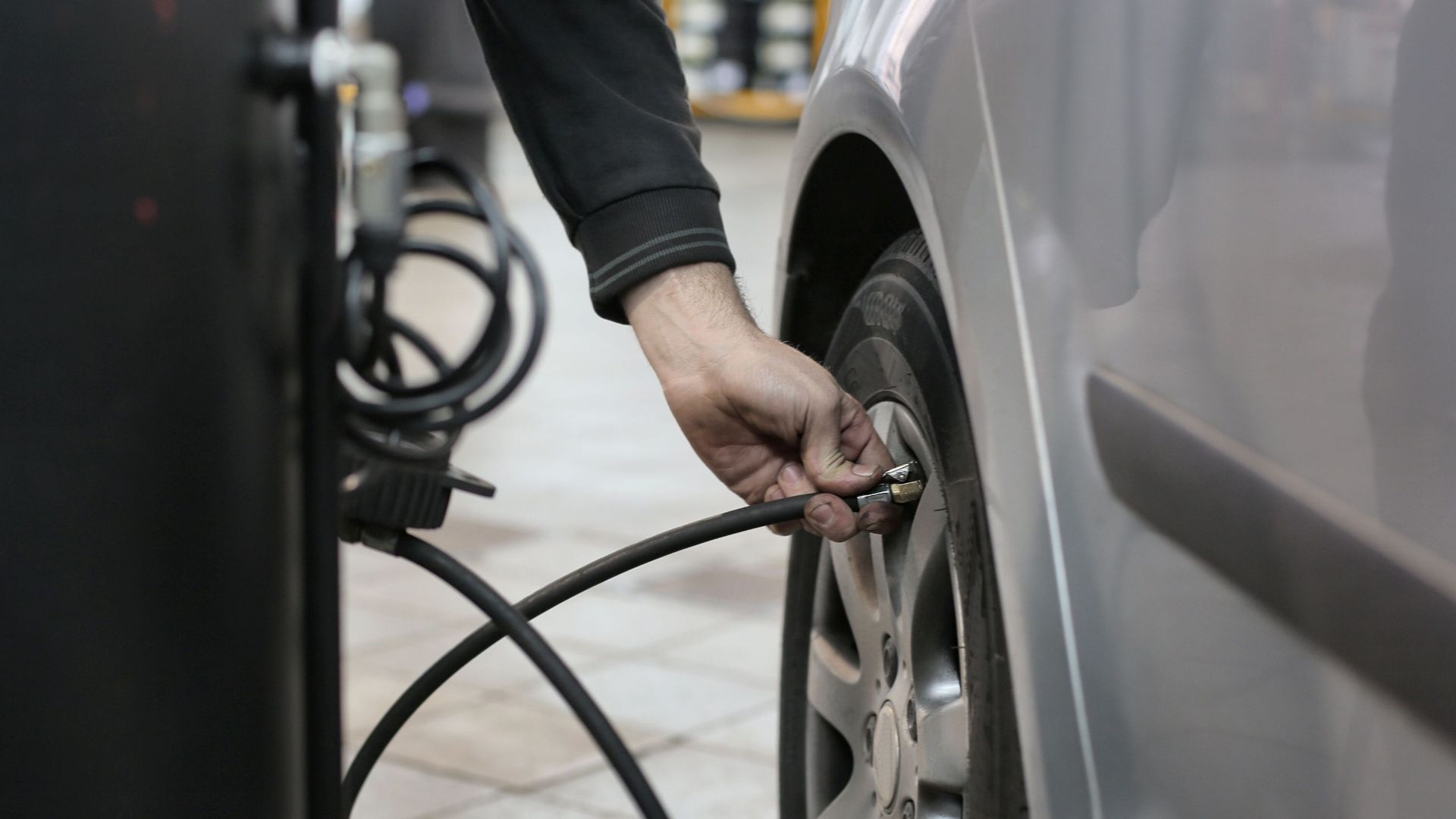 Mechanic inflating a car tire inside an auto repair shop, ensuring optimal tire pressure.