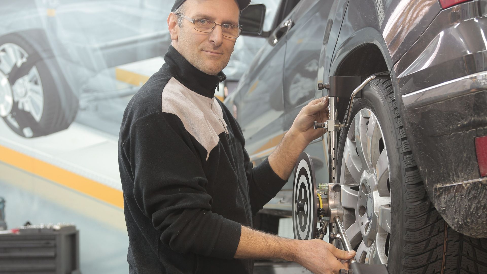 Mechanic performing wheel alignment on a car in a professional garage setting.