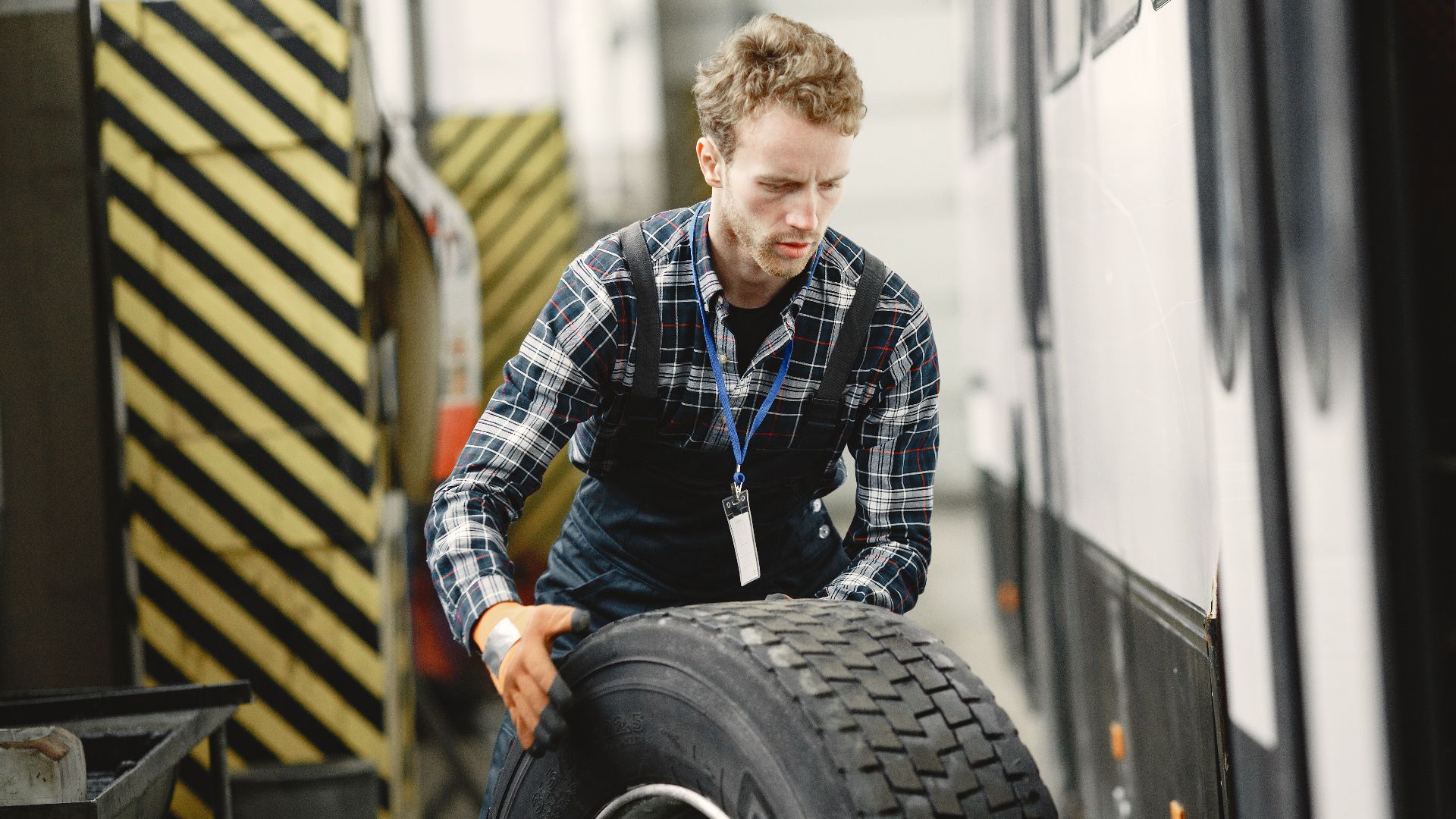 Auto mechanic working indoors in a vehicle repair garage managing a large tire.