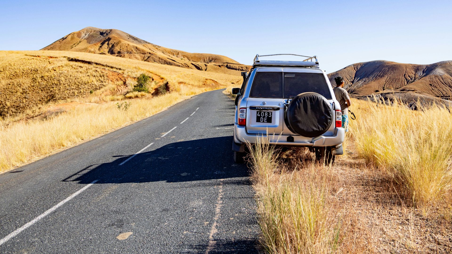 White suv parked on a desert road with dry hills.