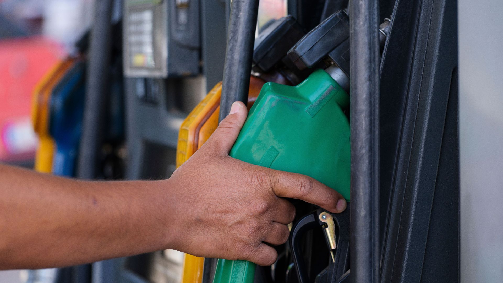 Close-up of a hand holding a green fuel nozzle at a gas pump station outdoors.