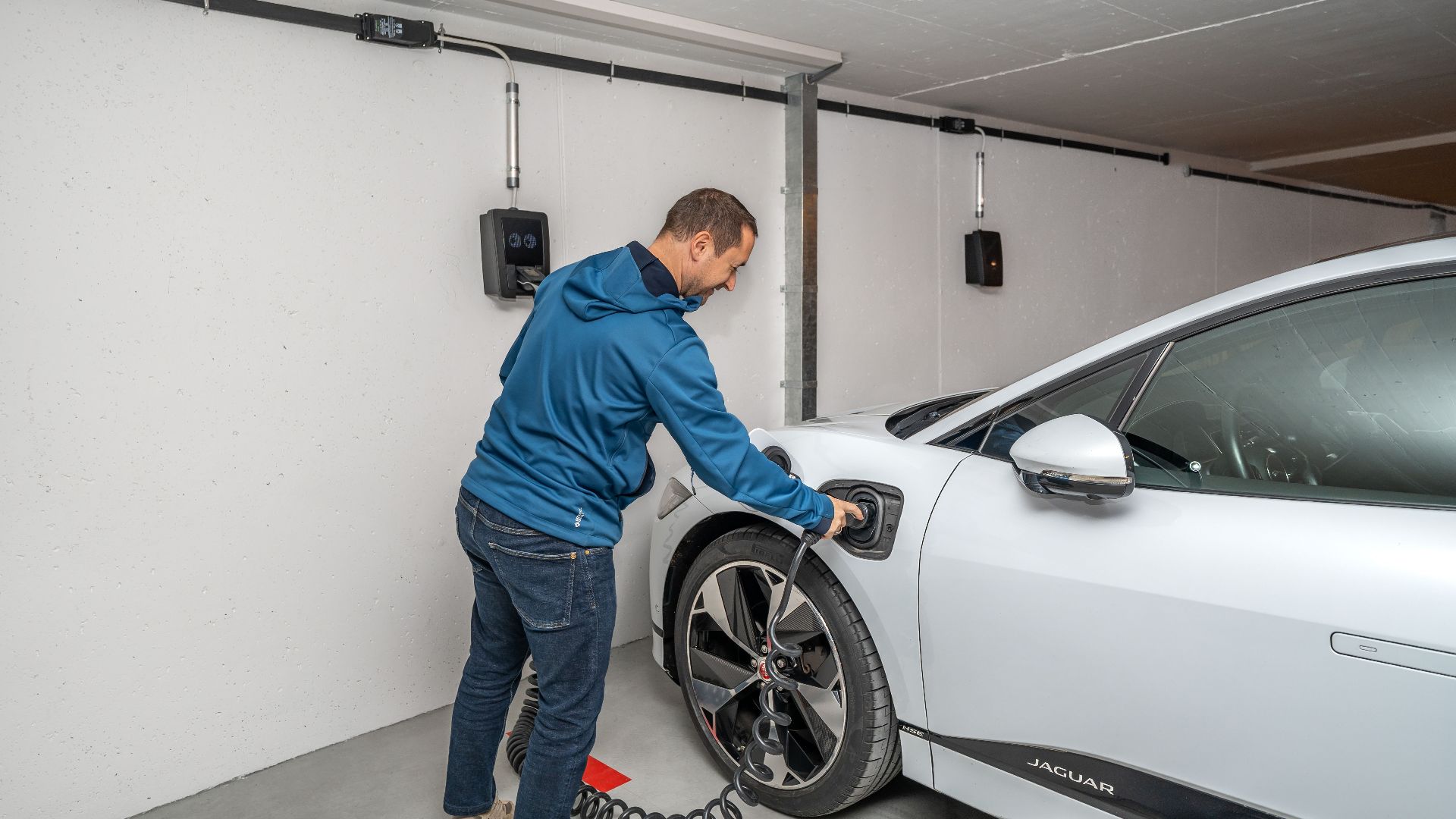 A man connects an electric car to a charging station in a modern indoor garage setting.