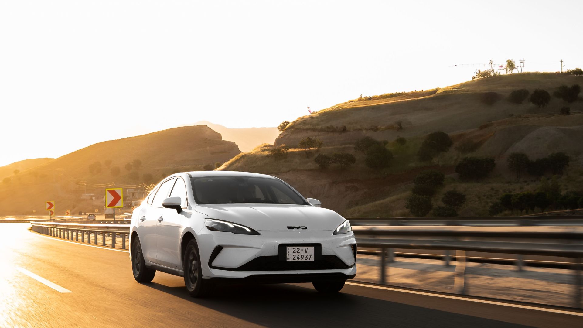 White electric car cruising on a sunlit highway, showcasing modern automotive design.