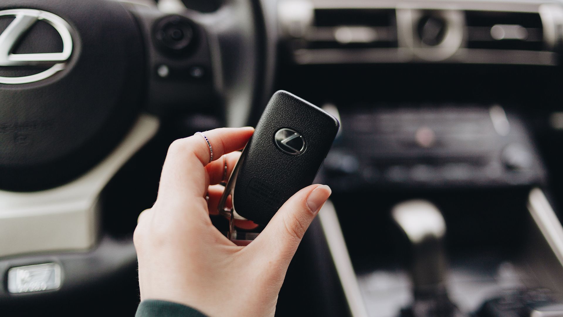 Person holding a Lexus car key inside a luxury vehicle's interior, showcasing brand elegance.
