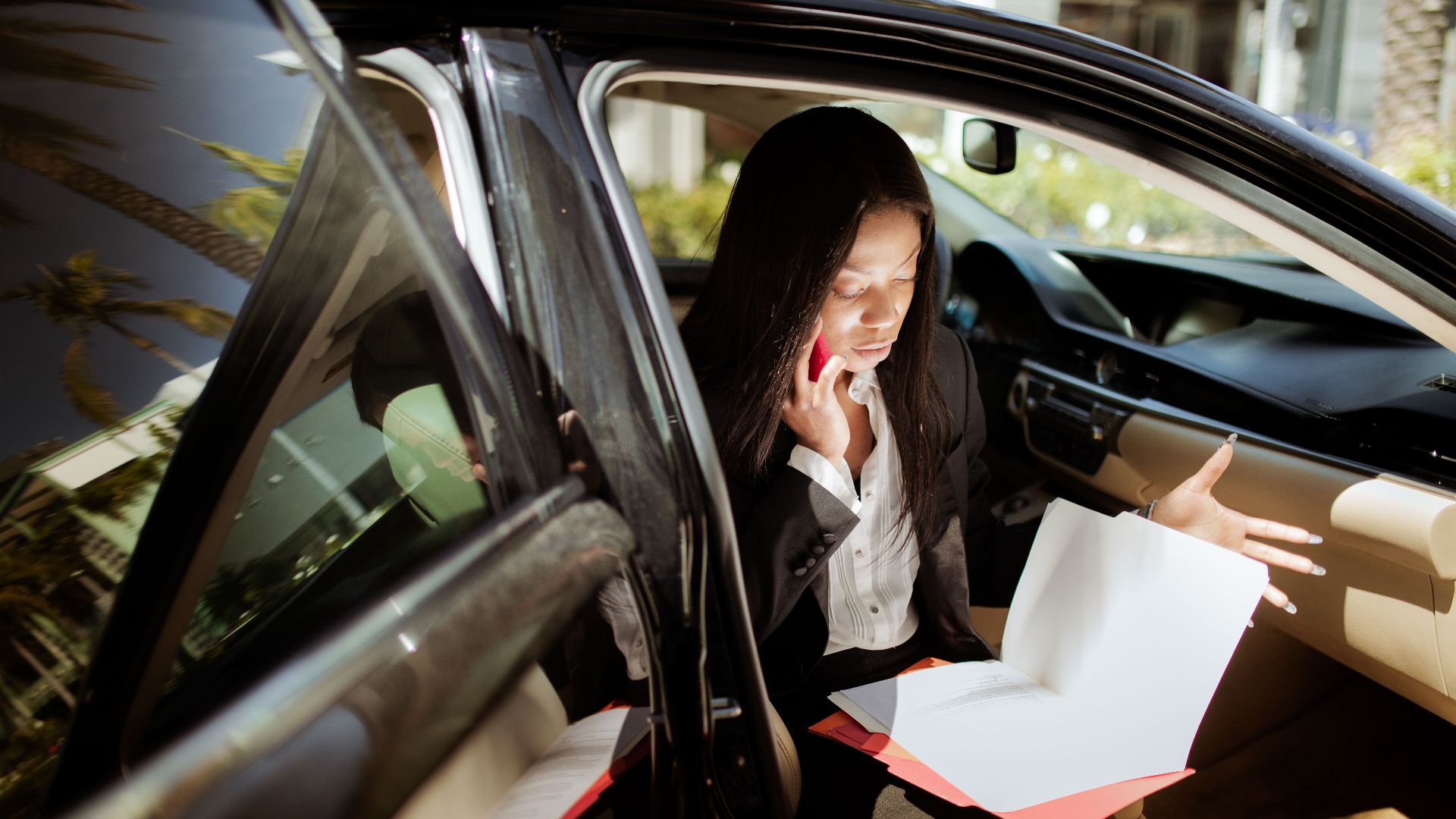 A businesswoman multitasking with phone and documents while seated in a car.