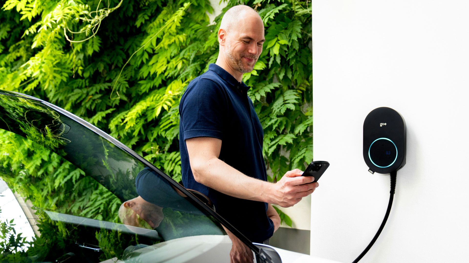 Man using phone near electric car charging station.