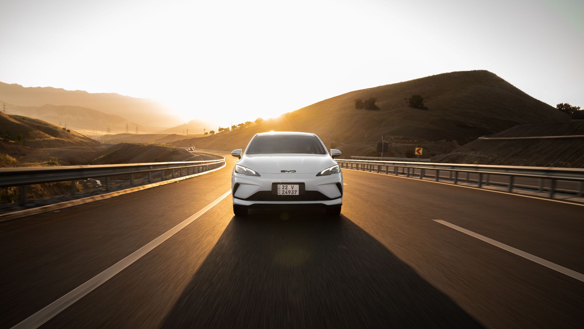 Electric car driving on a scenic highway at sunset, highlighting modern automotive design and sustainable travel.