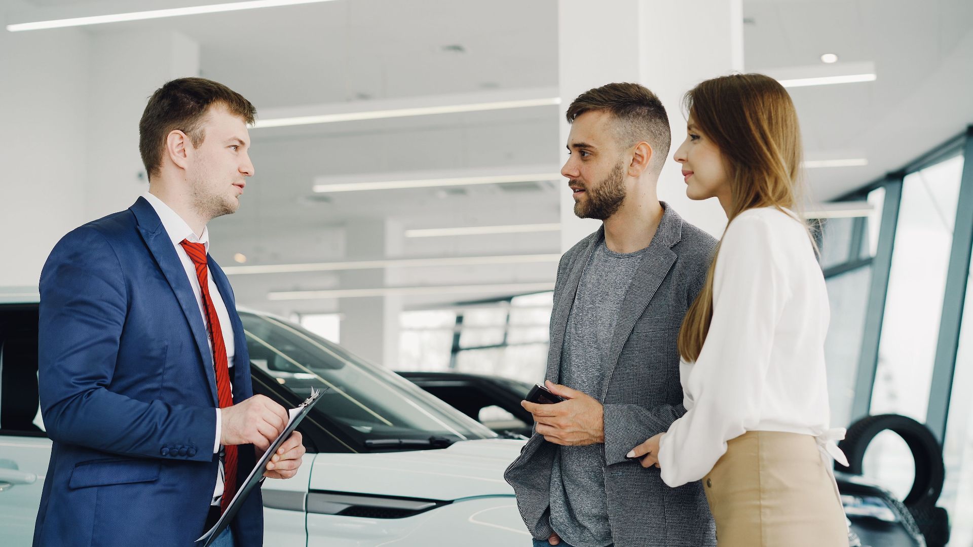 Car salesman assisting a couple in a modern showroom with a luxury car.