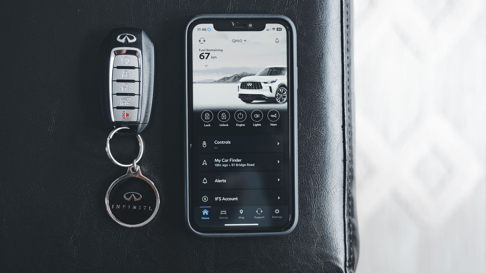 Close-up of an Infiniti key fob and smartphone displaying car app on a leather surface.