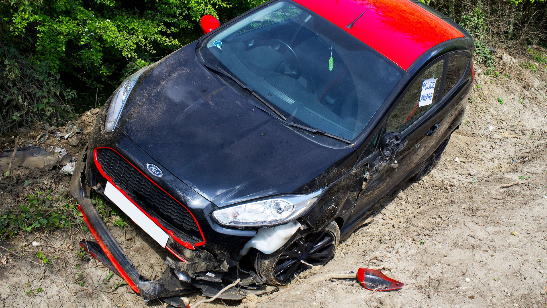 A black and red Ford Fiesta lies abandoned and damaged off-road in Welwyn Garden City, UK.