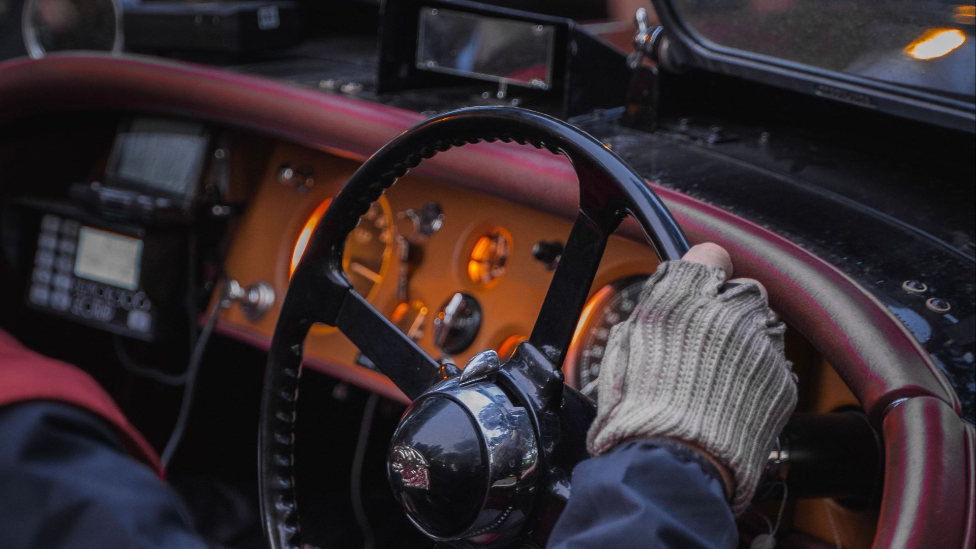 A close-up of a vintage car steering wheel with a gloved driver at the helm, highlighting classic automobile design.