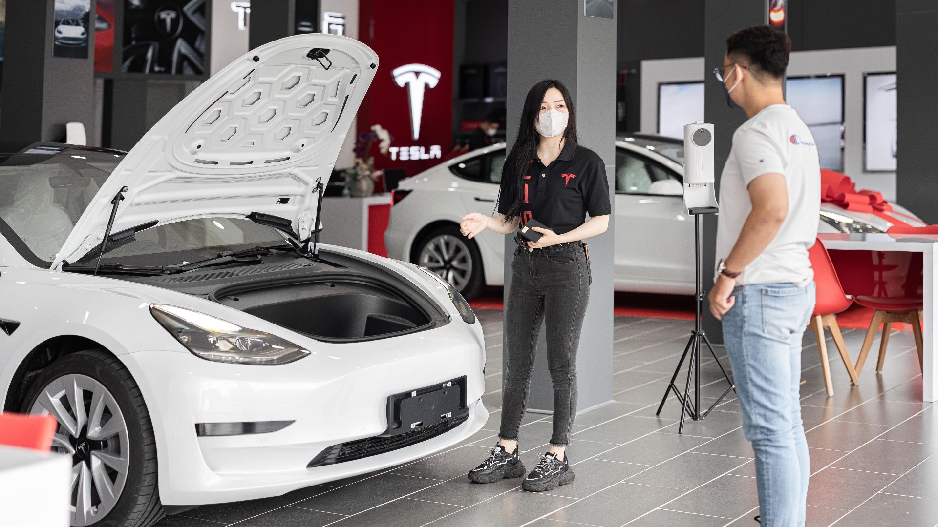 A customer talks with a sales representative about a Tesla Model 3 in a car dealership, showcasing the electric car's features.