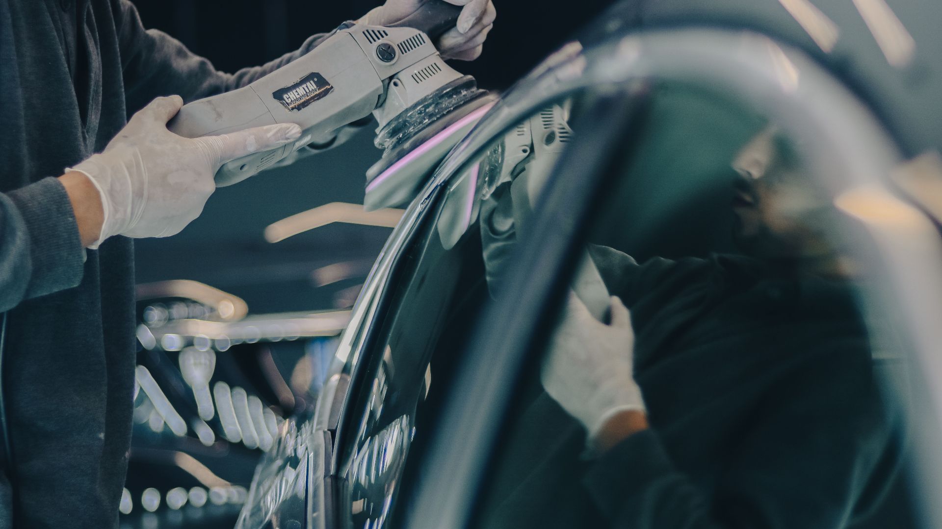 Close-up of car detailing process with polishing machine and reflective surface in workshop.