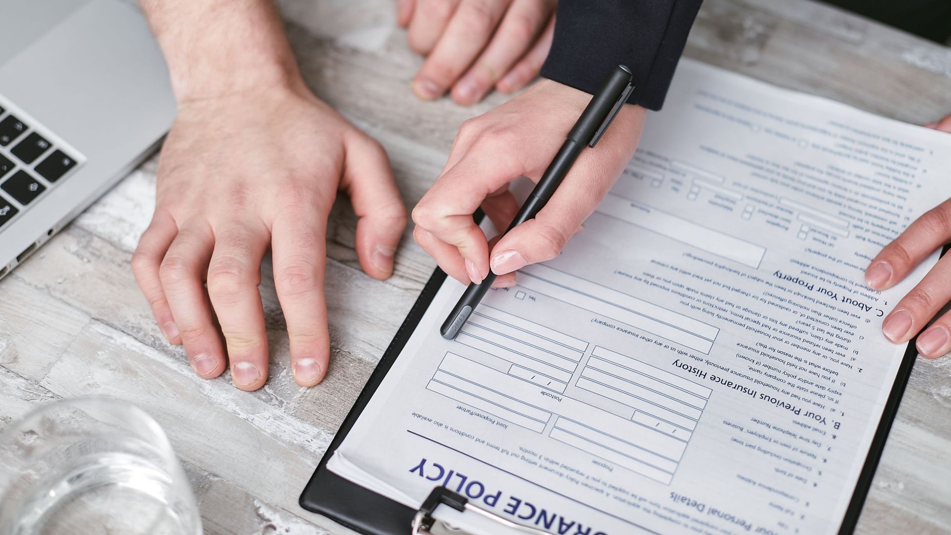 Close-up image of two people signing an insurance policy document on a wooden desk.