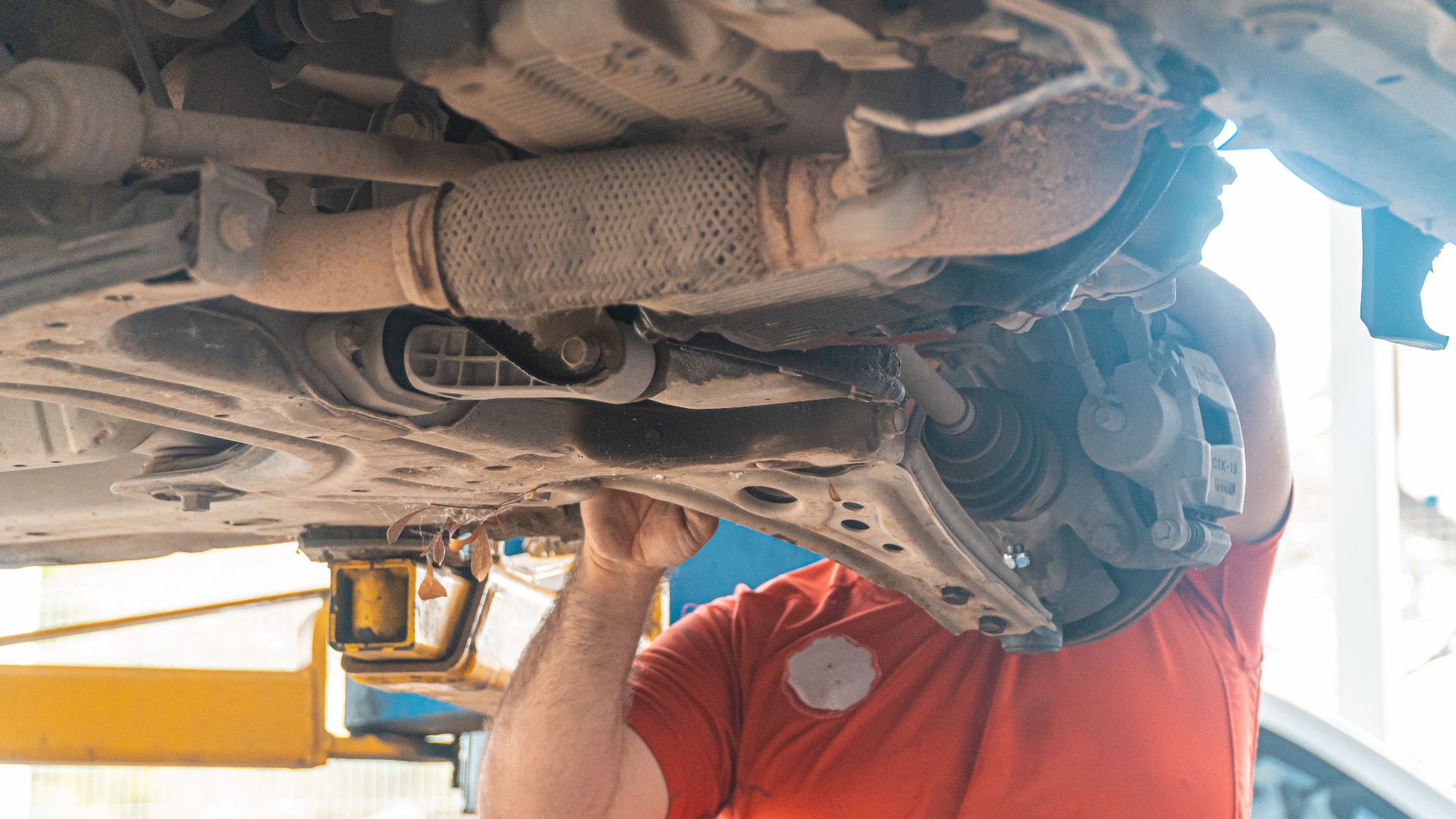 Mechanic working under a vehicle, inspecting the undercarriage in a repair garage, ensuring safety and performance.