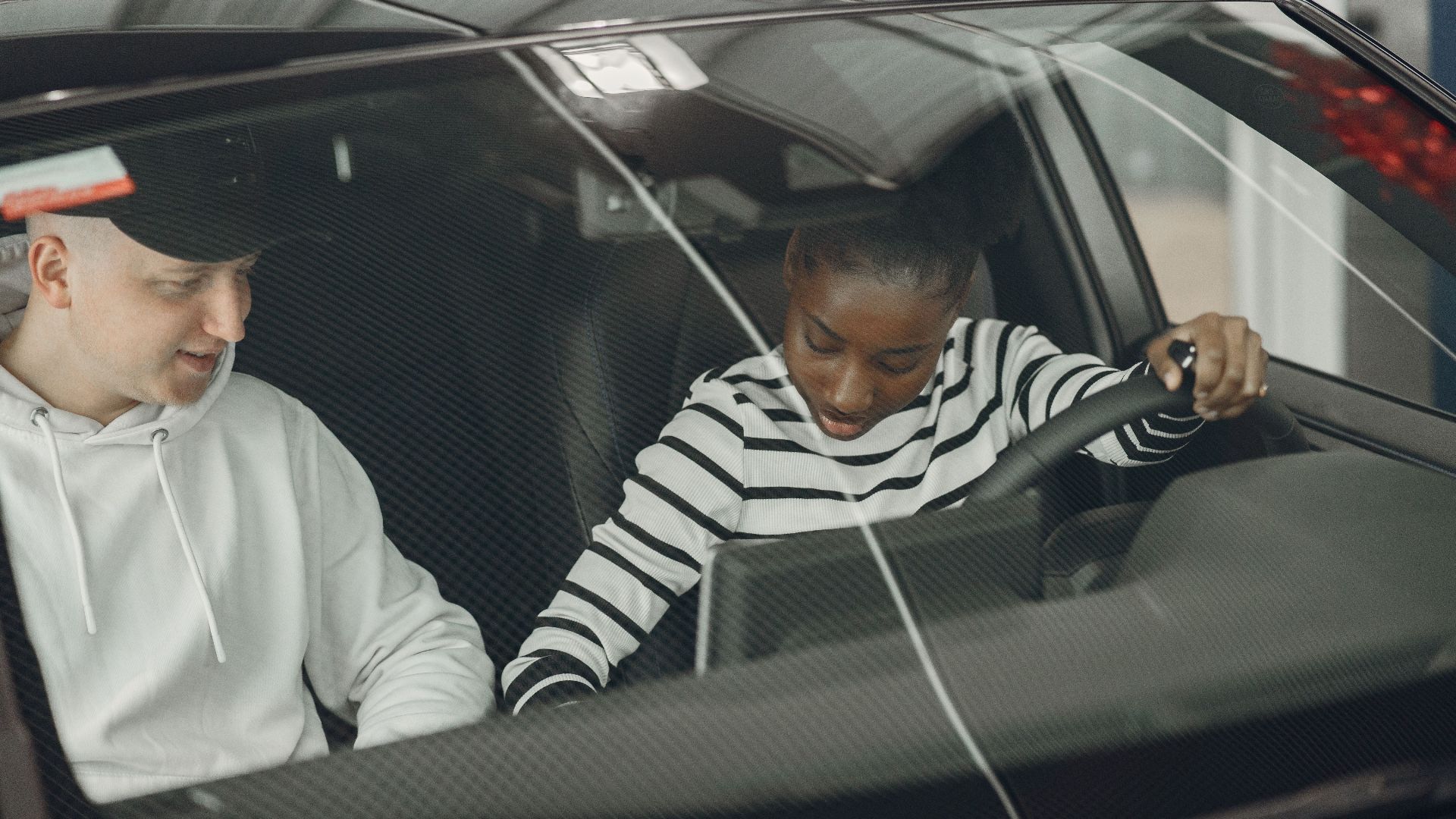 Black woman and caucasian man sitting inside a vehicle, discussing driving.