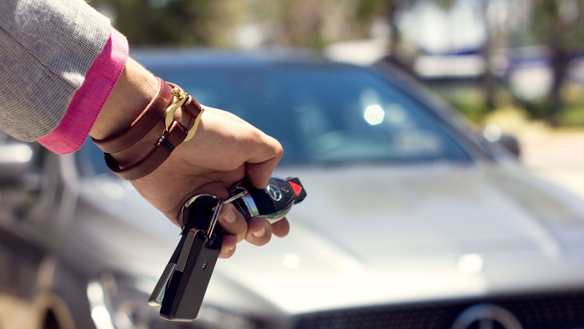 A close-up image of a hand holding car keys against the backdrop of a luxury car, outdoors.