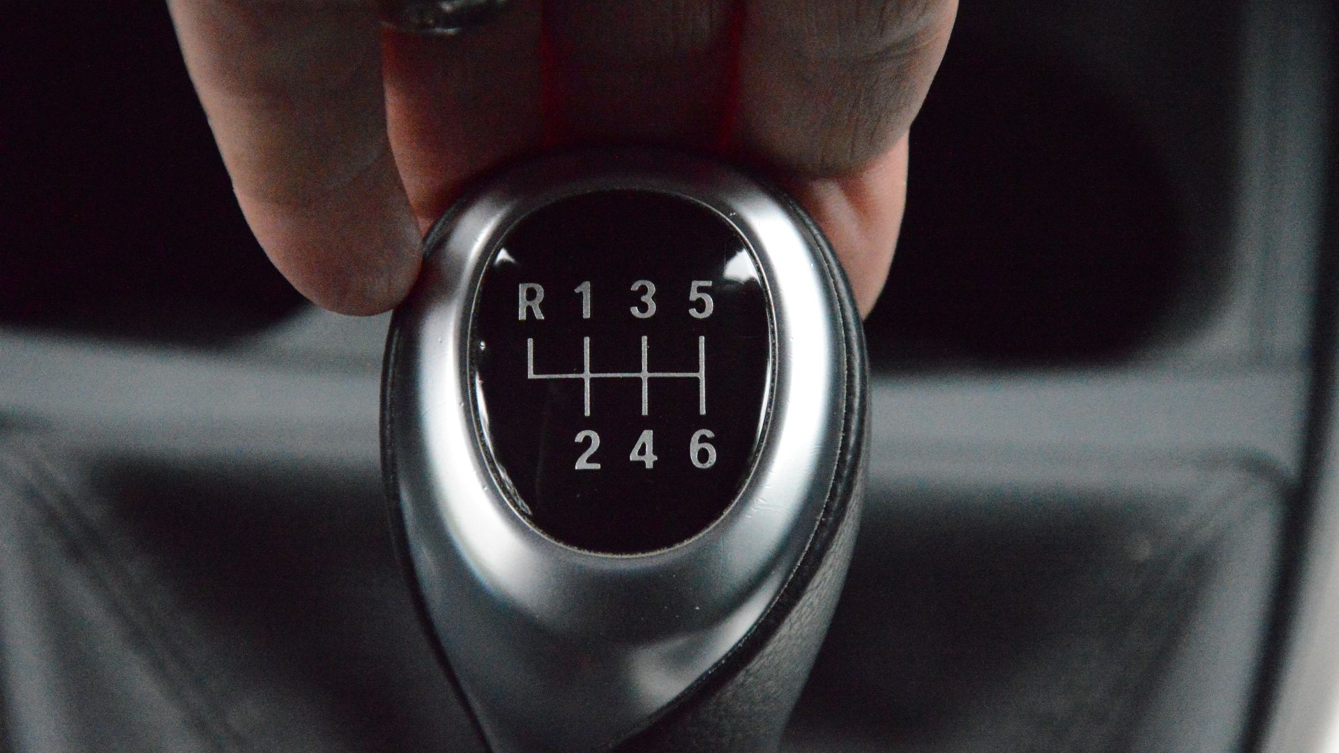 Detailed close-up of a hand operating a manual car transmission gear lever in a car interior.