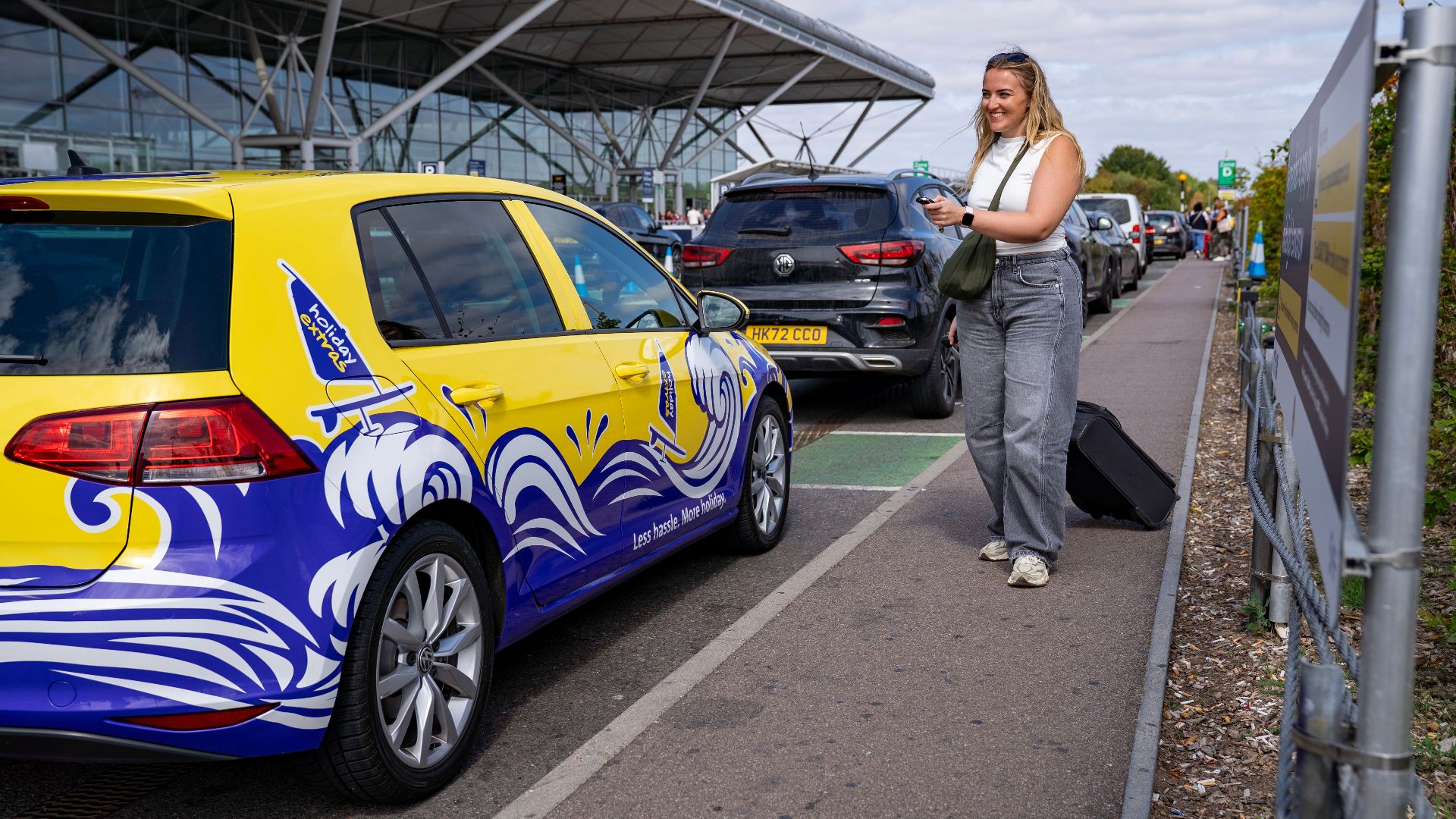 Woman smiling by a colorful car at Stansted Airport's valet parking area.