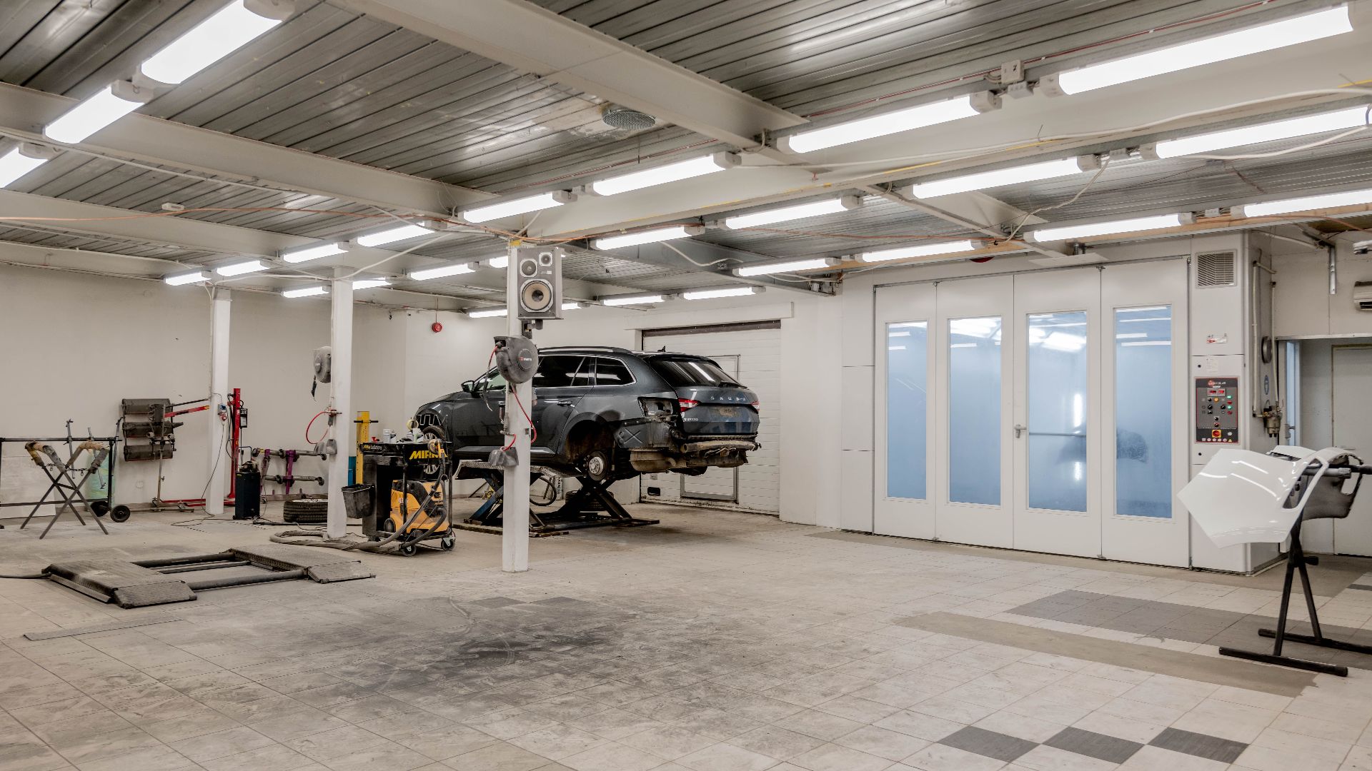 Interior view of a modern car repair garage with vehicle on lift and equipment.