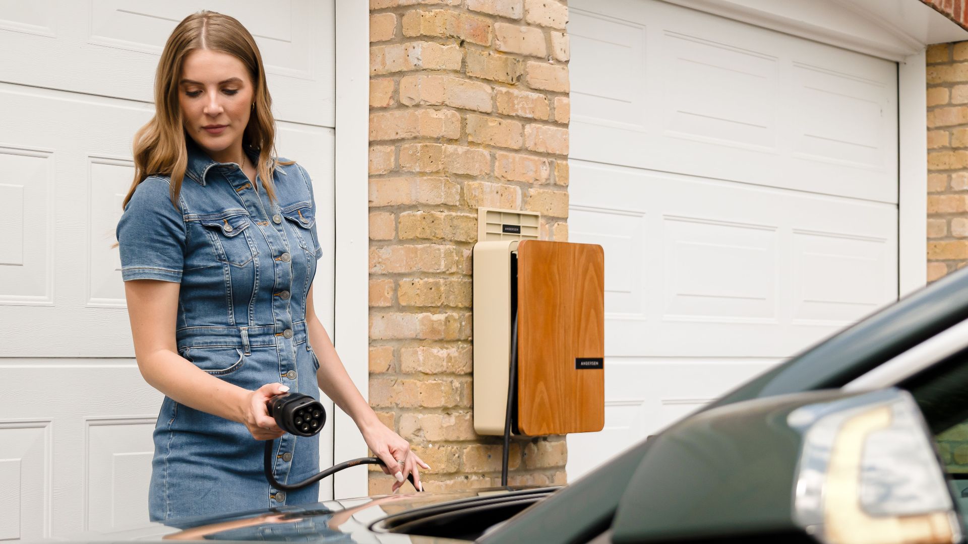 A woman plugs in an electric vehicle charger at a home charging station.