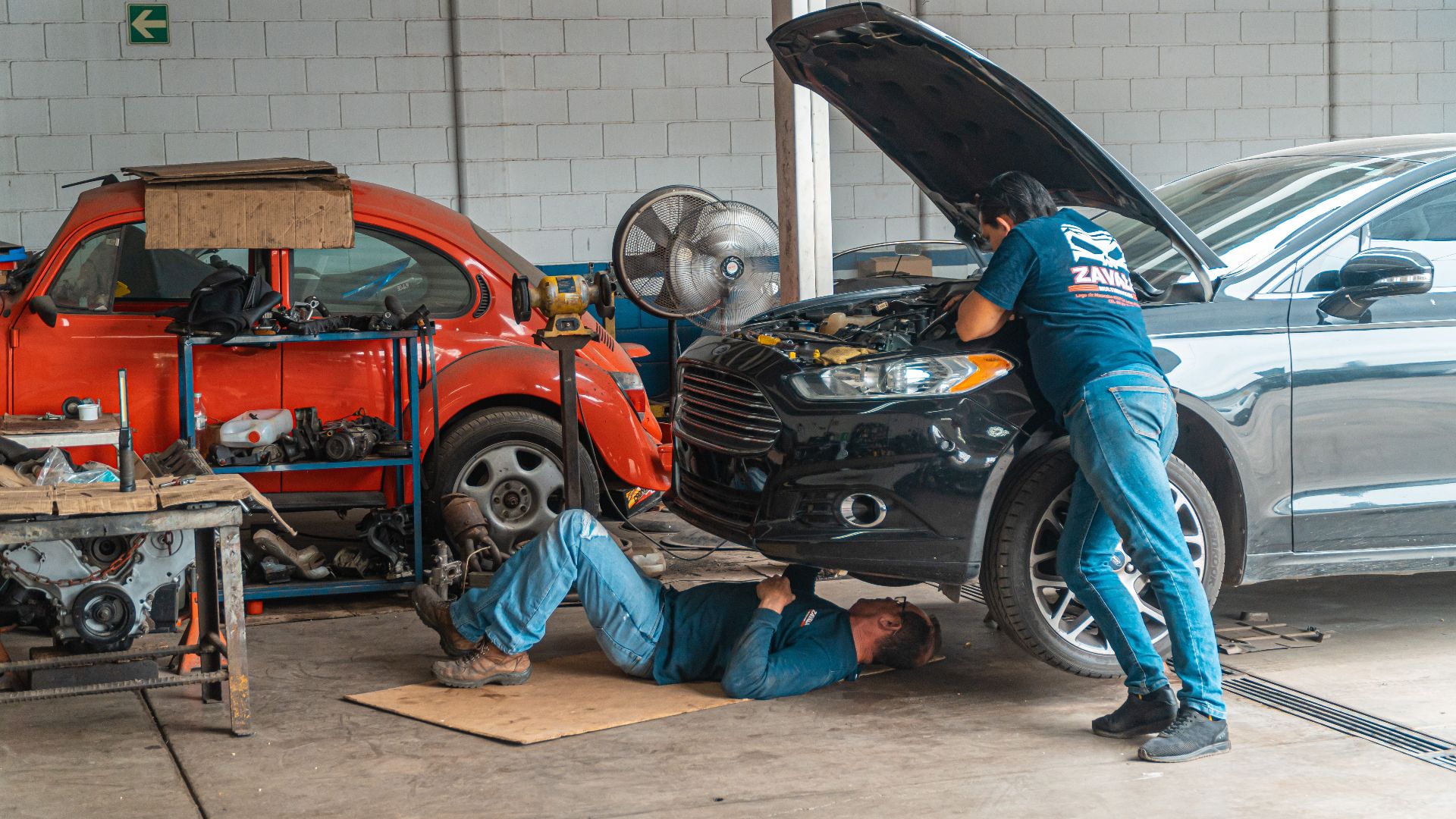 Mechanics working in an automotive workshop, repairing cars and performing maintenance.