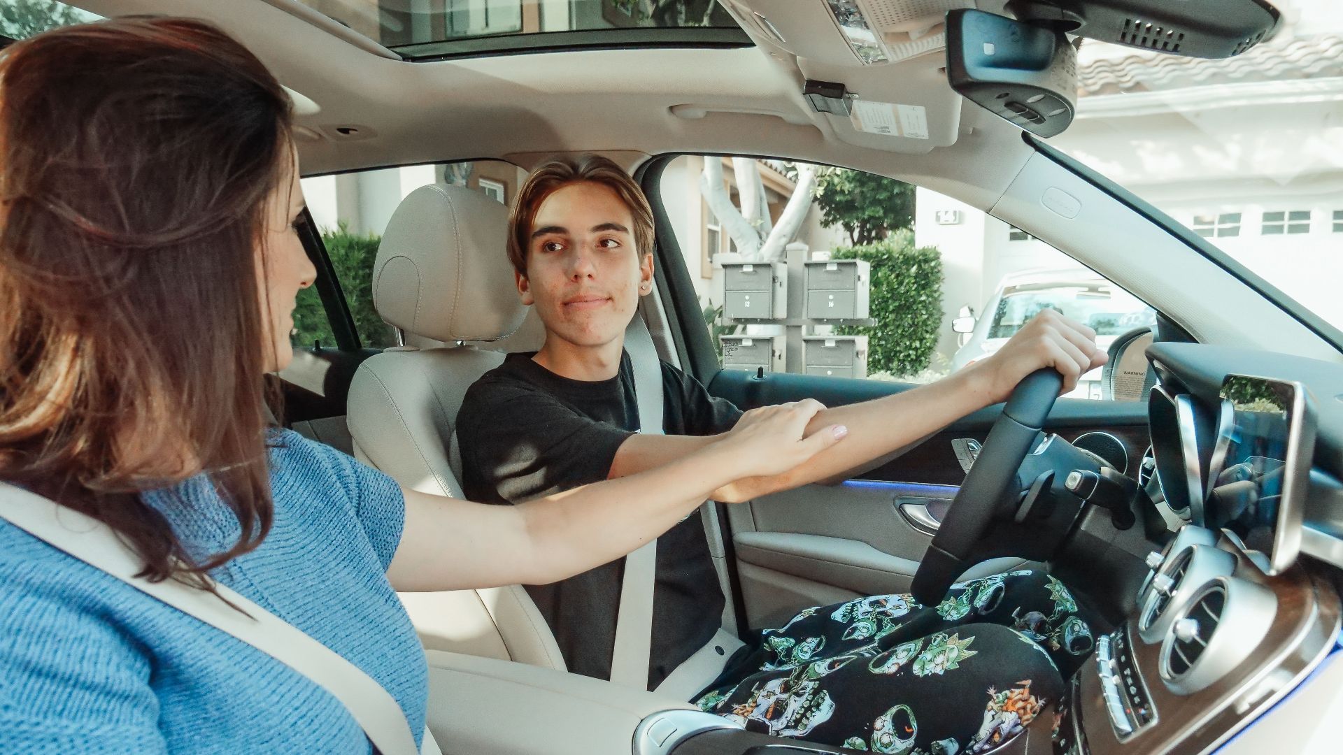 A mother supports her teenage son as he learns to drive in a car