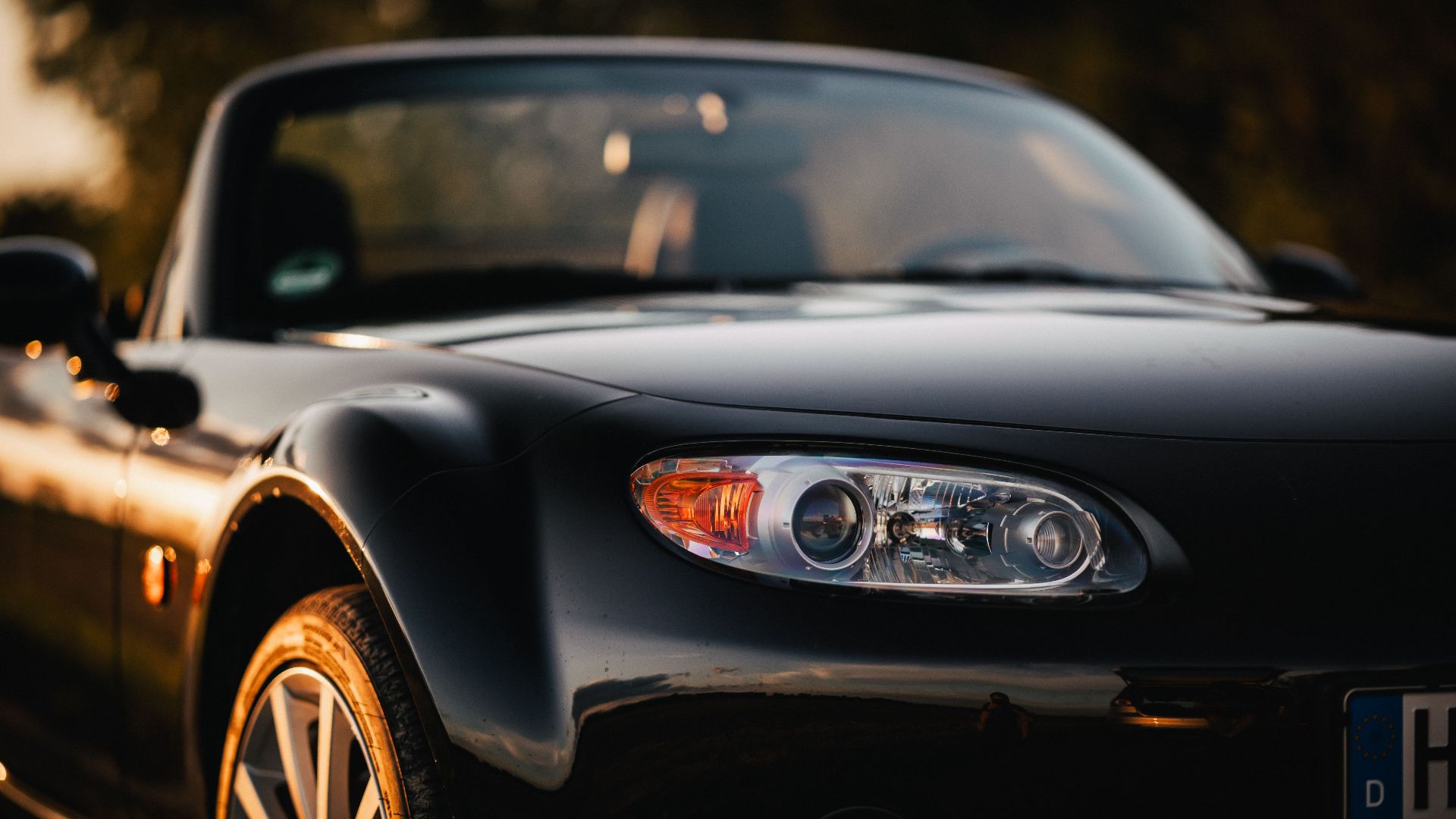 Close-up of a black Mazda MX-5 convertible reflecting sunset light, embodying modern automotive elegance.