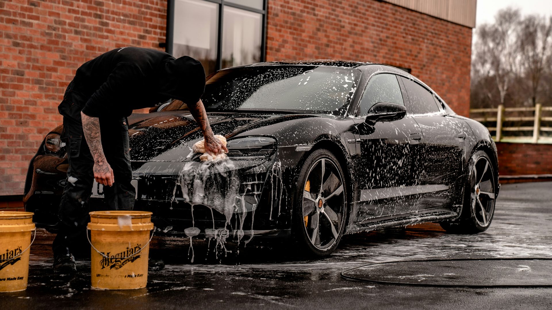 man in black t-shirt and black pants doing water splash on black coupe during daytime