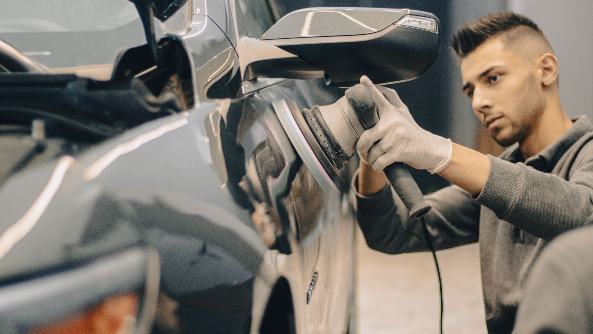 A focused worker polishes a vehicle with precision, enhancing its shine indoors.