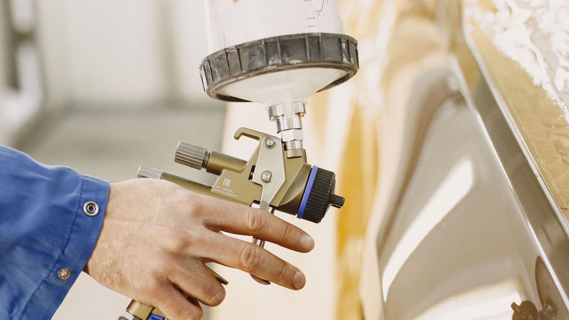 A technician spray paints a car with a paint spray gun in a workshop.