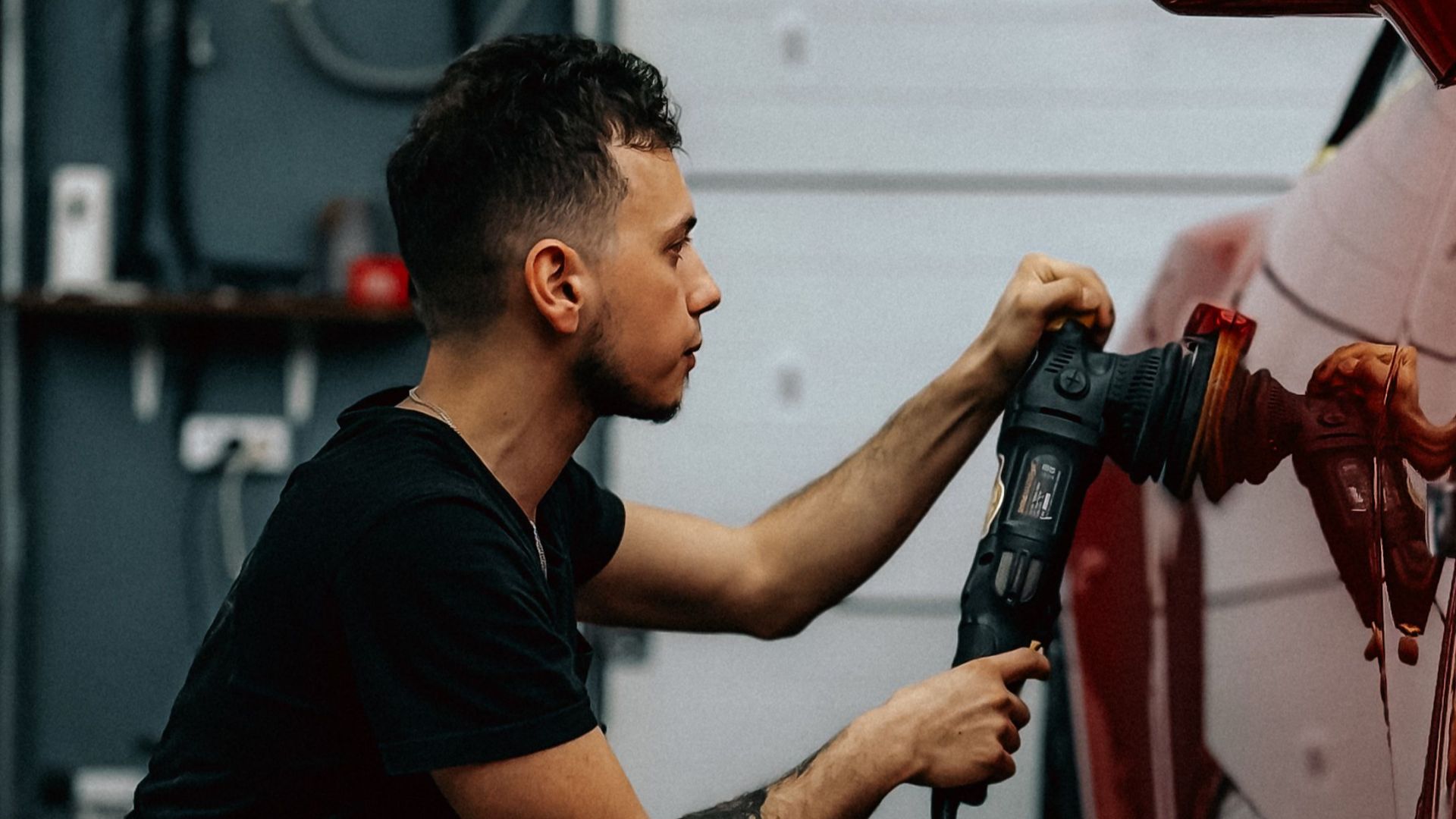 Man polishing a red sports car in a garage setting, demonstrating car detailing.