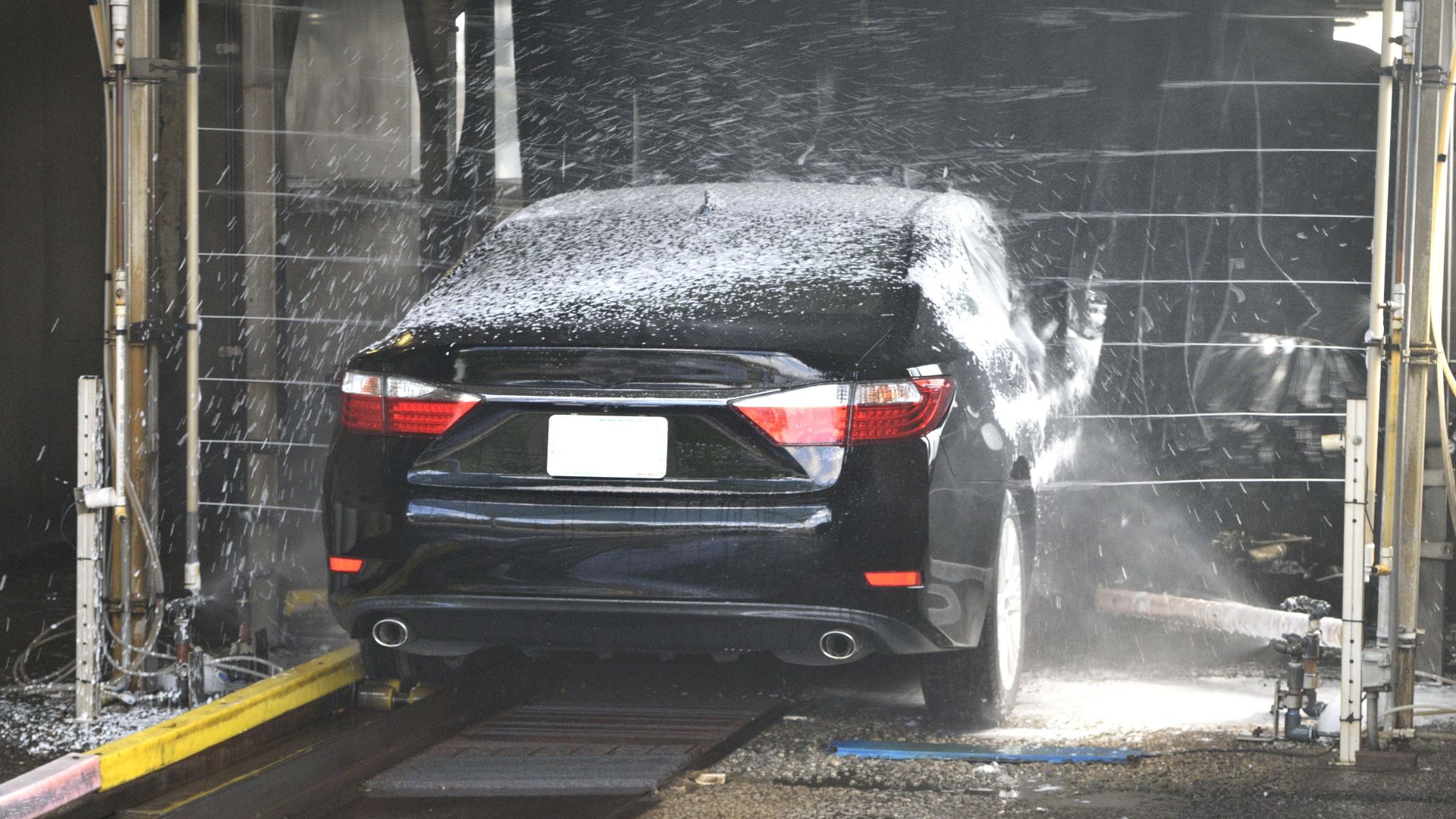 A black car being cleaned in an automated car wash with water and foam.