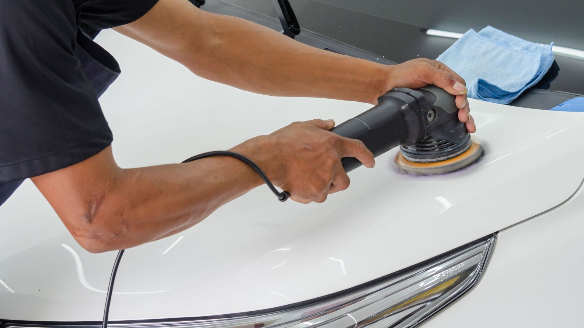 Close-up of a mechanic using a rotary polisher on a white car bonnet for detailing.