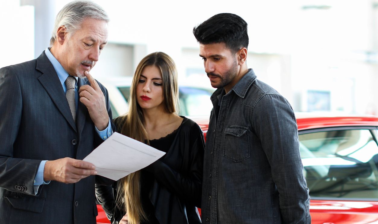 Car dealer reading a contract to a couple in an auto showroom