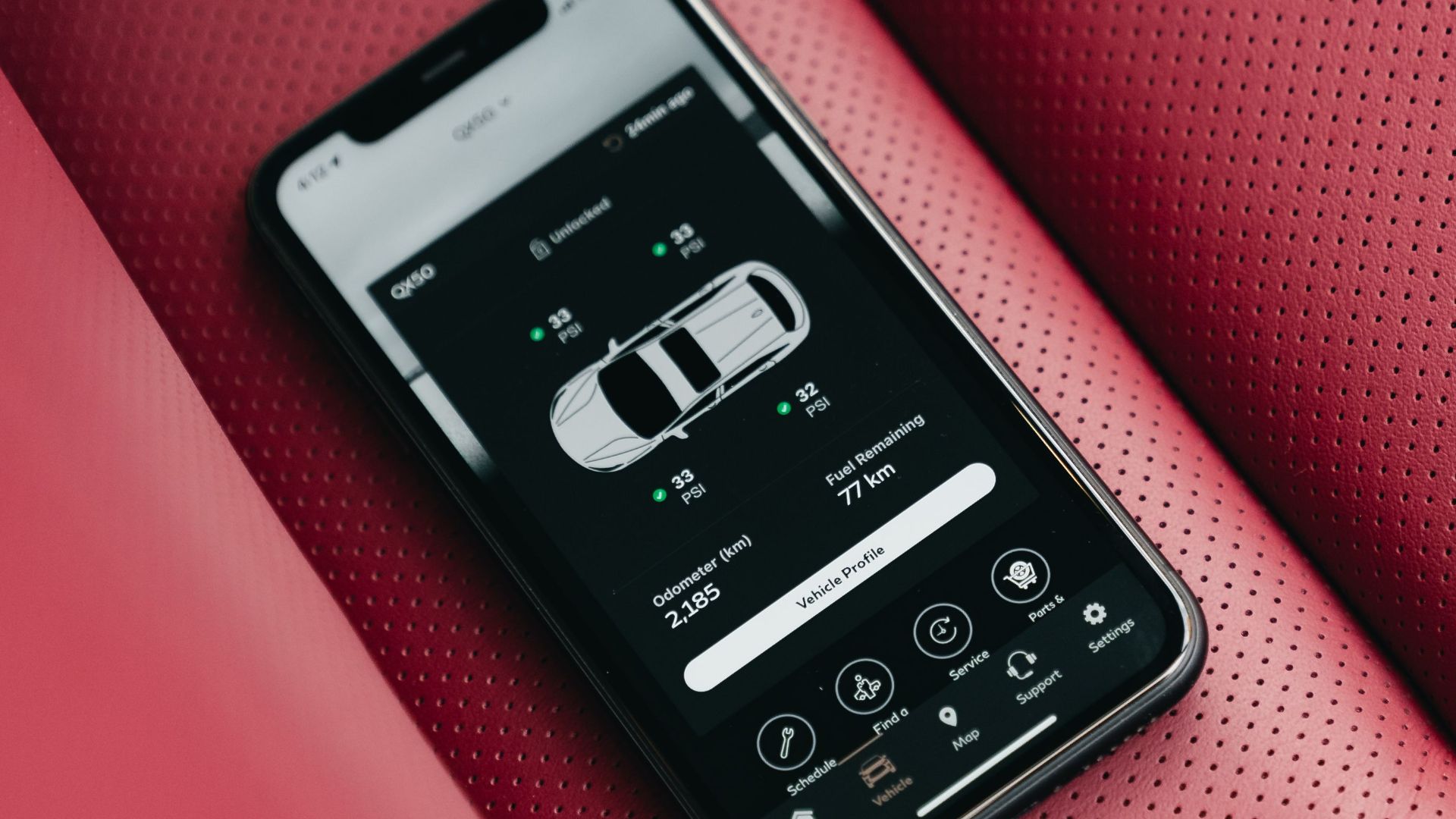 Smartphone showing car control app on red perforated leather car seat, close-up.