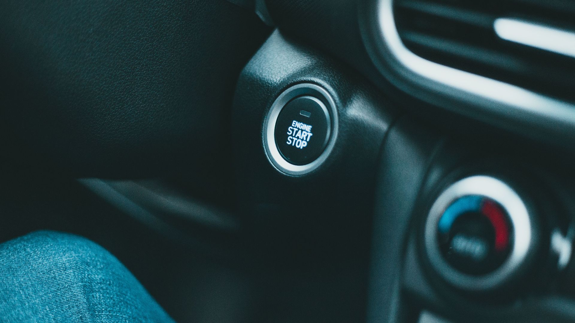 Closeup of black shiny dashboard with engine start button and conditioner controller of modern car in daylight