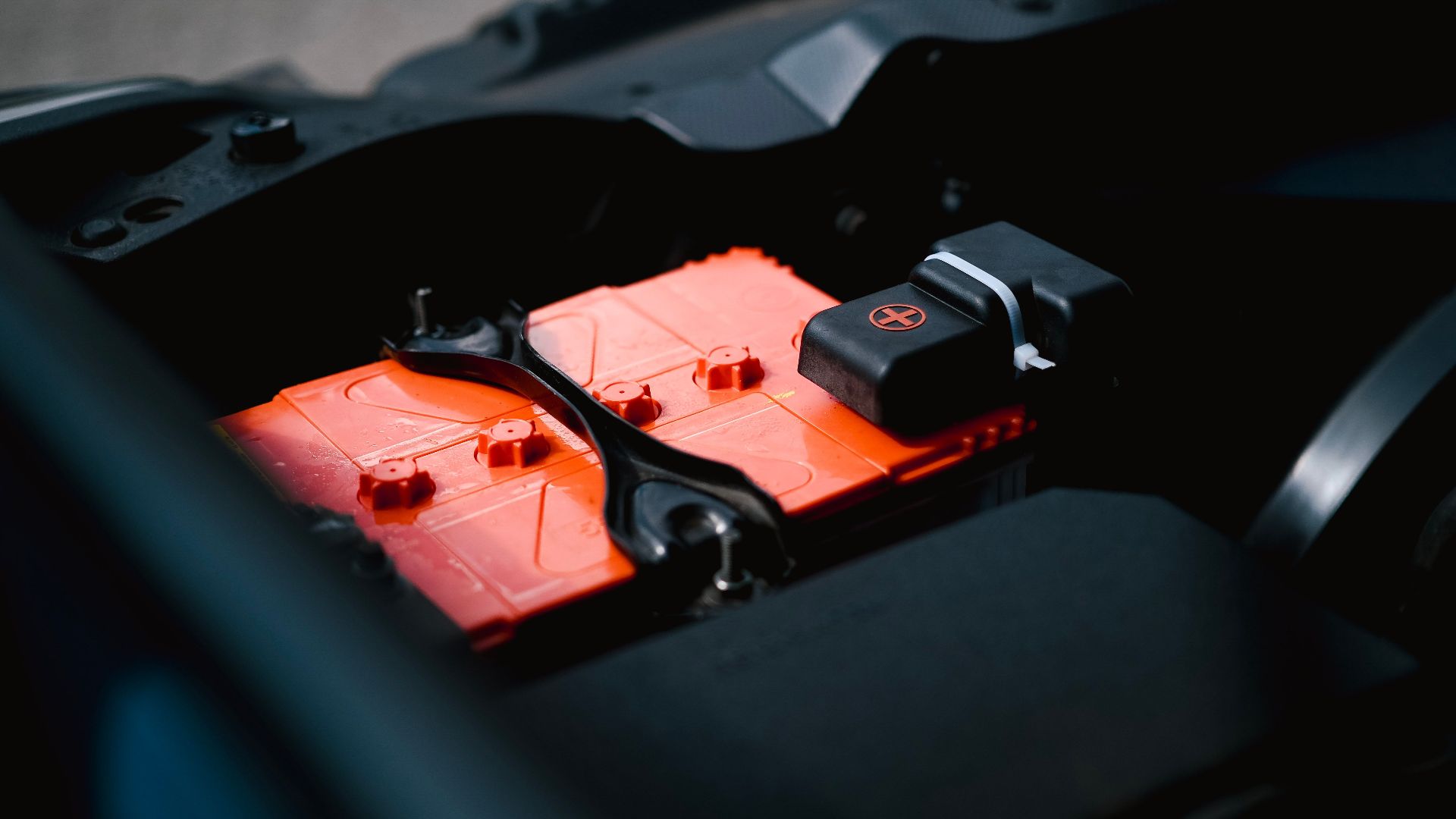 Detailed view of an orange car battery inside a vehicle's engine bay, highlighting its features.